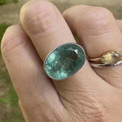 Bague cocktail pour femme en argent massif sertie d'une Aigue marine ovale facettée de couleur bleue verte. Pierre de 17 carats de qualité transparente avec inclusions naturelles. Bague réalisée en taille 60. Bijoux unique, éthique et durable présenté dans un coffret de notre marque, prêt à offrir. Livraison offerte, certificat d'authenticité, service client.
