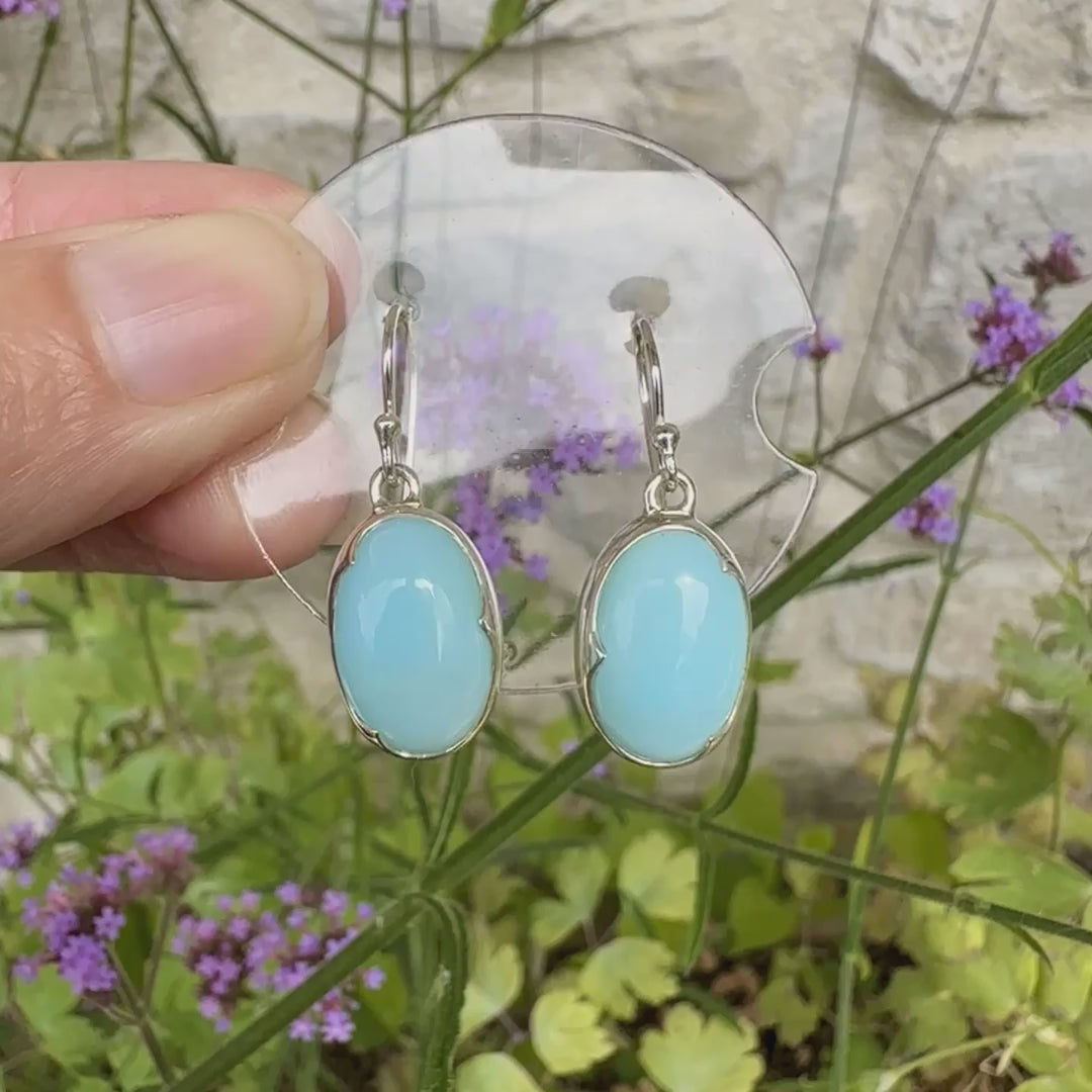 Boucles d'oreilles pendantes en argent massif serties d'opale bleue du Pérou. Pierres cabochon taillée en ovale de qualité opaque. Pierre naturelle de couleur bleu ciel. Bijoux unique, éthique et durable présenté dans un coffret de notre marque, prêt à offrir. Livraison offerte, certificat d'authenticité, service client.