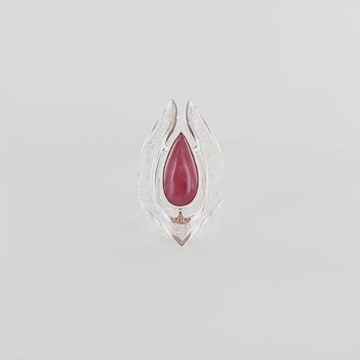 Vidéo d'une grande bague pour femme en argent massif sertie d'une Rhodonite. Pierre cabochon en forme de goutte, pierre naturelle de couleur rouge coquelicot. Pierre fine de qualité  opaque à translucide présentant des inclusions. Taille 59. Bijoux unique, éthique et durable présenté dans un coffret de notre marque, prêt à offrir. Livraison offerte, certificat d'authenticité, service client.