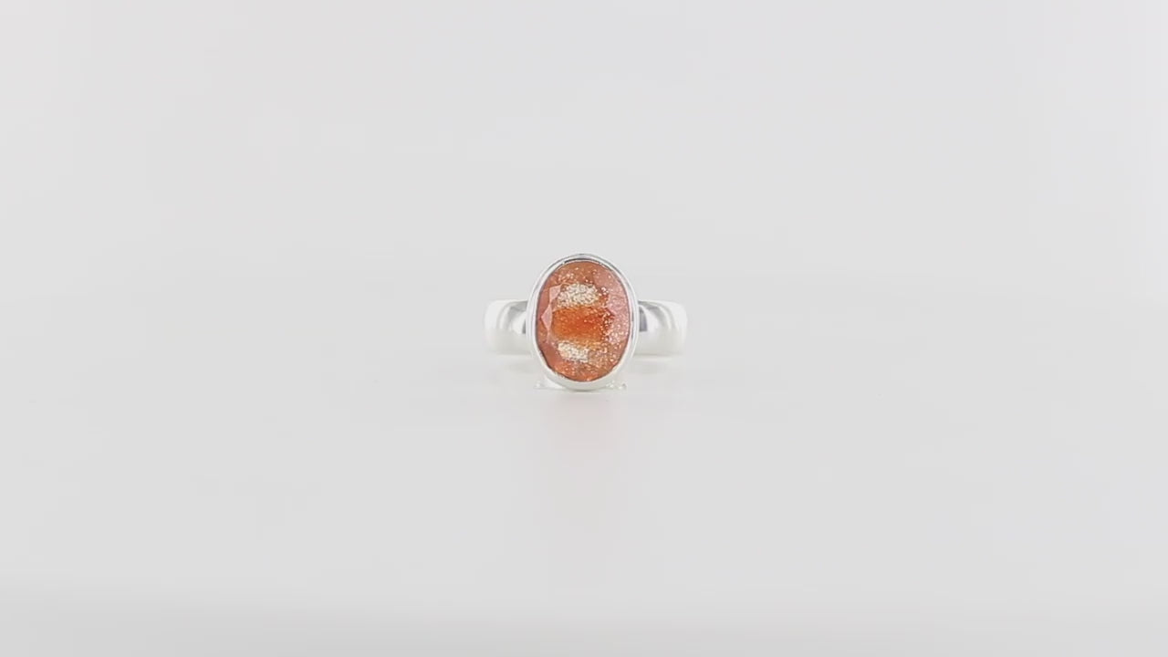 Bague pour femme en argent massif ornée d'une pierre de soleil ovale. La gemme présente une teinte orange-pêche chatoyante avec des inclusions scintillantes dorées caractéristiques. Montée sur un large anneau en argent poli. Bague réalisée en taille 59. Bijoux unique, éthique et durable présenté dans un coffret de notre marque, prêt à offrir. Livraison offerte, certificat d'authenticité, service client.