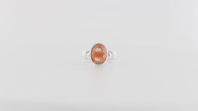 Bague pour femme en argent massif ornée d'une pierre de soleil ovale. La gemme présente une teinte orange-pêche chatoyante avec des inclusions scintillantes dorées caractéristiques. Montée sur un large anneau en argent poli. Bague réalisée en taille 59. Bijoux unique, éthique et durable présenté dans un coffret de notre marque, prêt à offrir. Livraison offerte, certificat d'authenticité, service client.