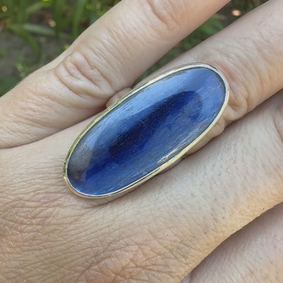 Bague pour femme en argent massif sertie d'un long cabochon ovale de cyanite bicolore de couleur bleu jean nacré. Pierre translucide à inclusions. Bijou unique réalisée en taille 54 par Orchajewelry