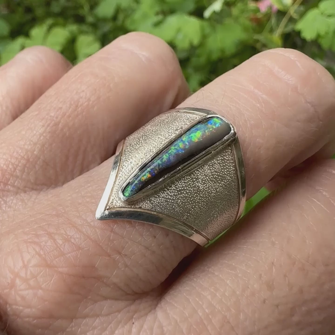 Bague pour femme en argent massif 925 sertie d'une opale boulder aux feux multicolores bleus violet et verts. Cabochon d'opale massive naturelle taillée en forme d'aile. Pierre de qualité opaque. Bijoux unique réalisé en taille 58 par Orcha Jewelry.