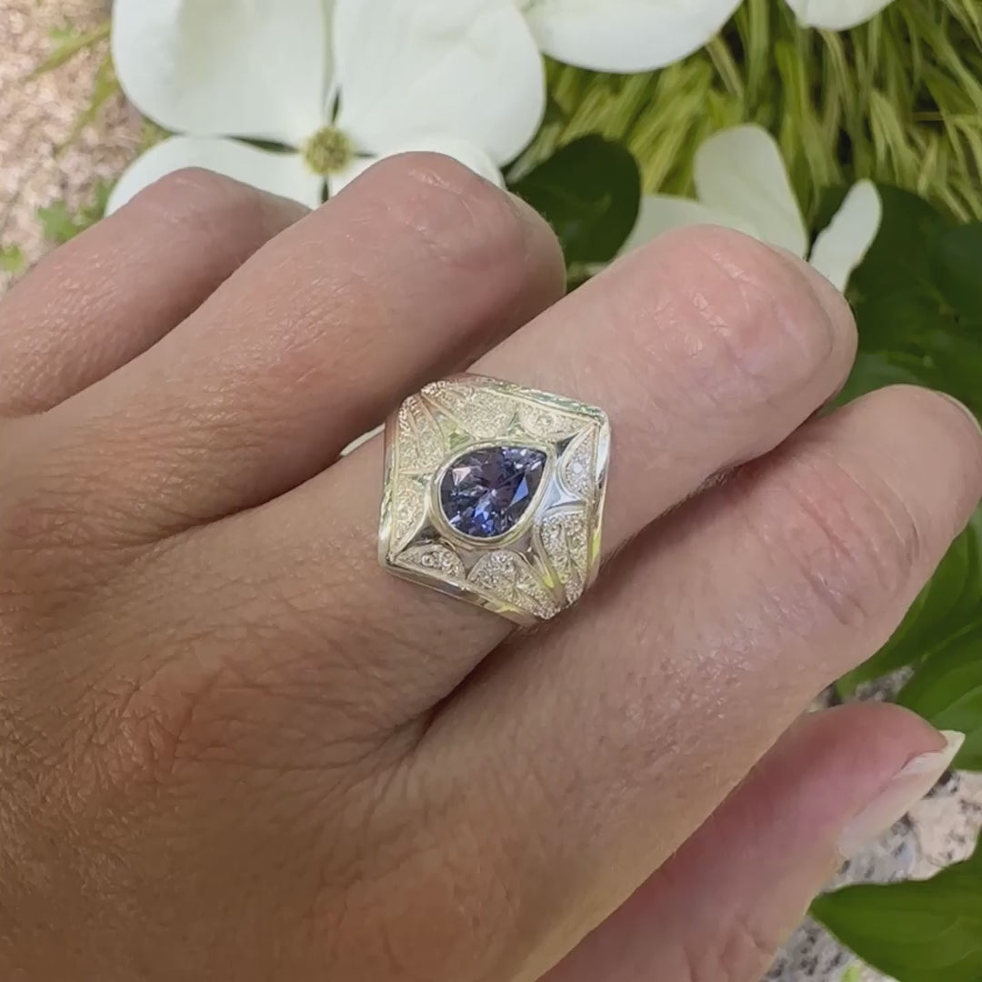Video d'une bague pour femme en argent massif sculptée d'étoiles et autres corps célestes sertie d'une Tanzanite de couleur bleu lavande. Pierre naturelle, facettée en forme de forme goutte, de qualité transparente présentant un très bel éclat. Taille 58. Bijoux unique, éthique et durable présenté dans un coffret de notre marque, prêt à offrir. Livraison offerte, certificat d'authenticité, service client.
