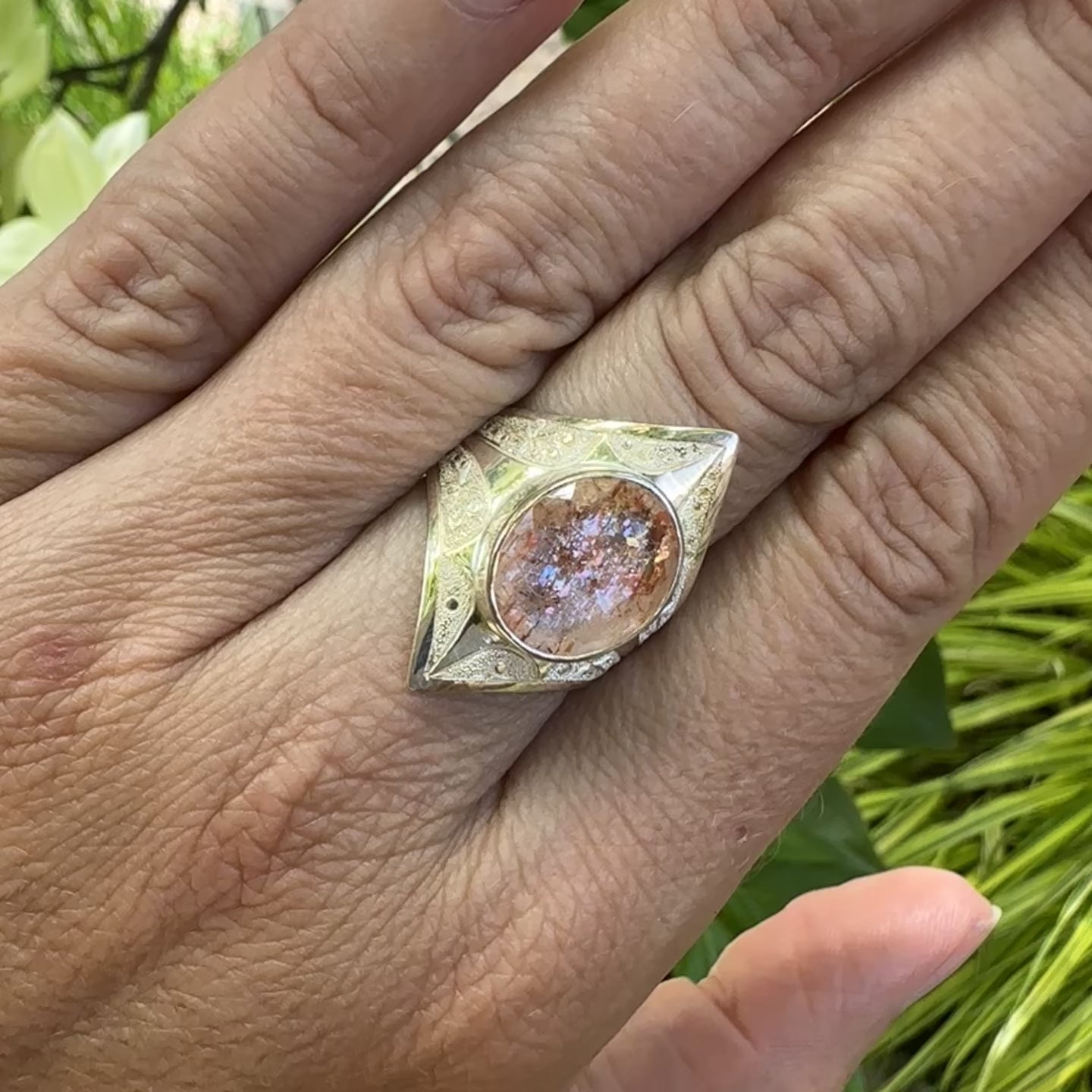 vidéo d'une bague pour femme en argent massif sculptées d'étoiles et autres corps célestes sertie d'une pierre de soleil aux nuances orangées rouges scintillantes. Pierre naturelle, facettée de forme ovale, de qualité transparente pierre transparente avec inclusions scintillantes d'hématites. Taille 59. Bijoux unique, éthique et durable présenté dans un coffret de notre marque, prêt à offrir. Livraison offerte, certificat d'authenticité, service client.