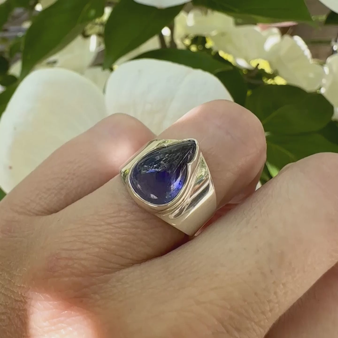 Vidéo d'une grande Bague pour femme en argent massif, sertie d'un cabochon de tanzanite bleu lavande. Pierre taillée en forme de goutte. Pierre transparente comportant des inclusions. Taille 54. Bijoux unique, éthique et durable présenté dans un coffret de notre marque, prêt à offrir. Livraison offerte, certificat d'authenticité, service client.