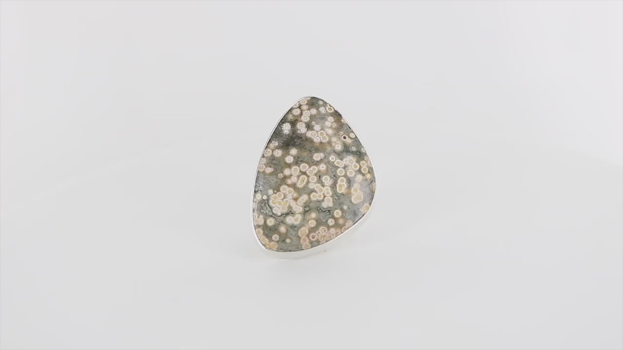 Bague contemporaine pour femme en argent massif, ornée d’une grande pierre triangulaire polie : un jaspe océan. La gemme présente un fond gris-vert moucheté de cercles crème et beige, rappelant des bulles ou des coraux sous-marins. Bague réalisée en taille 59. Bijoux unique, éthique et durable présenté dans un coffret de notre marque, prêt à offrir. Livraison offerte, certificat d'authenticité, service client.