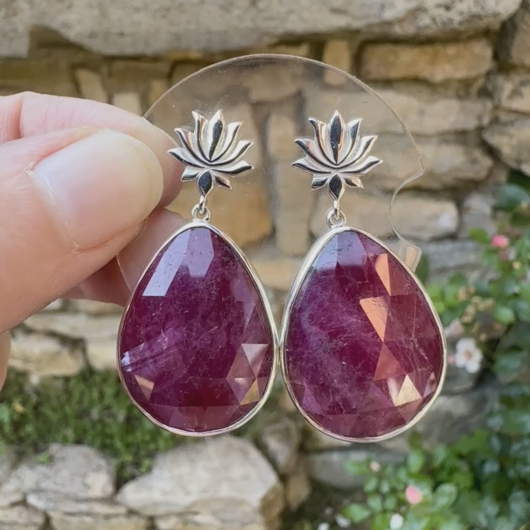 Boucles d'oreilles lotus pour femme en argent massif sertie de rubis. Cabochons facettés en forme de goutte de qualité opaque. Pierre naturelle de couleur rouge violacé. Le clou des boucles représente un lotus. Bijoux unique, éthique et durable présenté dans un coffret de notre marque, prêt à offrir. Livraison offerte, certificat d'authenticité, service client.
