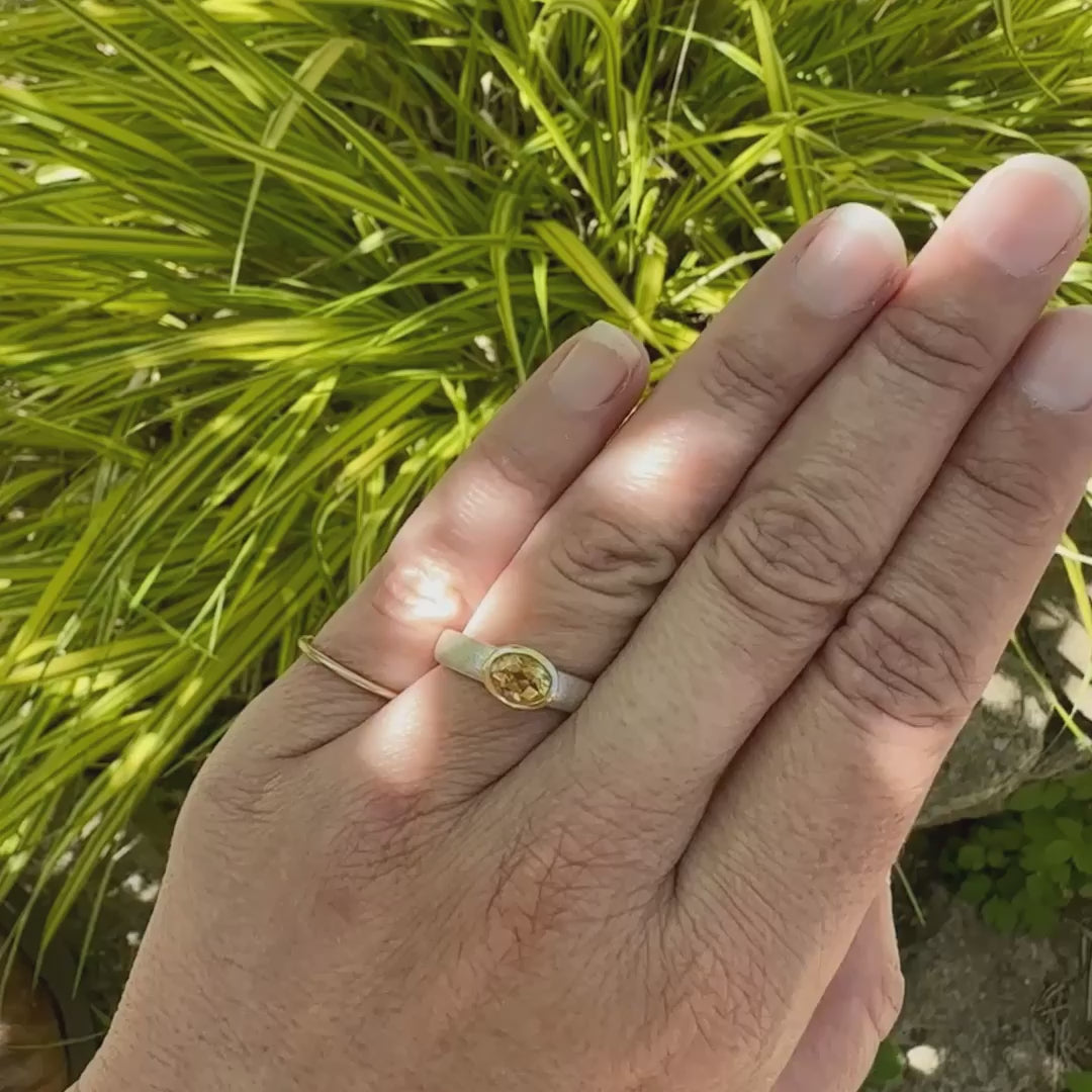 Vidéo sur une main d'une bague anneau pour femme en argent massif et or sertie d'une Citrine. Pierre facettée de forme ovale, de qualité transparente, propre à l'oeil. Pierre naturelle de couleur jaune doré lumineux. Bijoux unique, éthique et durable présenté dans un coffret de notre marque, prêt à offrir. Livraison offerte, certificat d'authenticité, service client.
