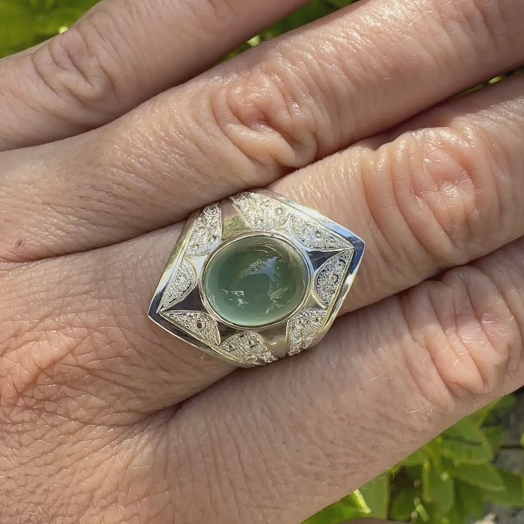 Bague pour femme en argent massif sculptées d'étoiles et autres corps célestes sertie d'un cabochon ovale de préhnite de couleur verte pastel lumineuse. Pierre naturelle de qualité transparente présentant des inclusions. Bijoux unique réalisé en taille 57 par Orchajewelry.