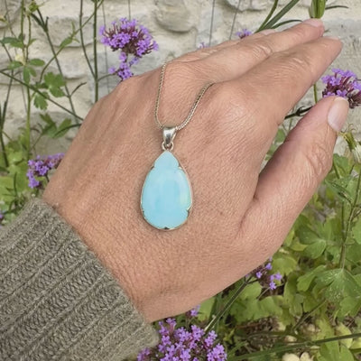 photo sur modèle d'un pendentif en argent massif, sertie d'un cabochon d'opale bleue du Pérou de couleur bleu ciel clair. Pierre en forme de goutte. Pierre opaque et translucide. Bijoux unique, éthique et durable présenté dans un coffret de notre marque, prêt à offrir. Livraison offerte, certificat d'authenticité, service client.