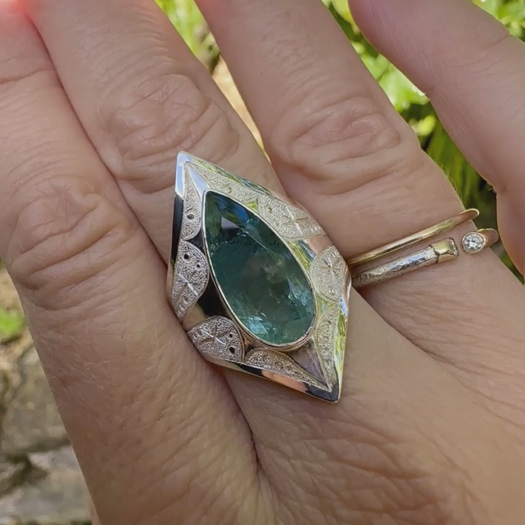 Bague pour femme en argent massif sculptées d'étoiles et autres corps célestes sertie d'une Aigue marine. Pierre facettée en forme de goutte, pierre naturelle aux nuances de bleus . Qualité  transparente avec inclusions, pierre naturelle n'ayant subit aucun traitement. Taille 60.5. Bijoux unique, éthique et durable présenté dans un coffret de notre marque, prêt à offrir. Livraison offerte, certificat d'authenticité, service client.

