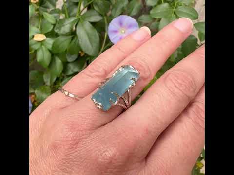 Bague cocktail pour femme en argent massif sertie d'une aigue marine taillée de 15 carats de couleur bleue gris trouble, pierre transparente avec inclusions. Pierre naturelle facettée de forme rectangulaire. Bijoux unique réalisée en taille 54,5 par Orchajewelry 