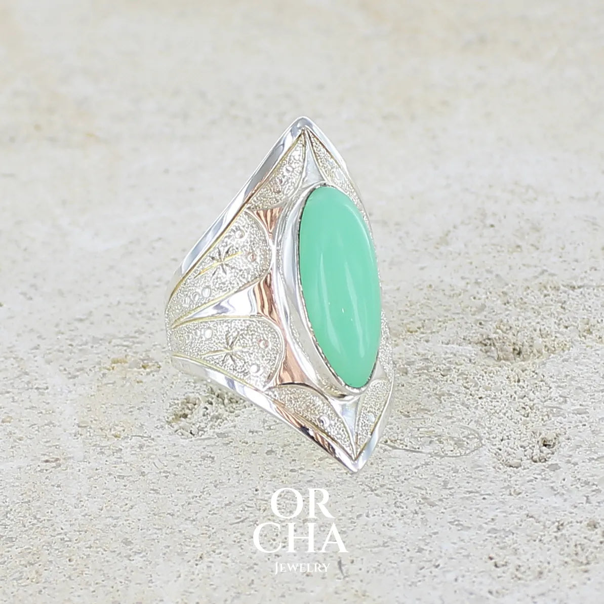 Profil droit d'une bague marquise pour femme en argent massif sculptées d'étoiles et autres corps célestes sertie d'un cabochon de chrysoprase de couleur verte pastel. Pierre naturelle de qualité translucide taillée en ovale longiligne. Bague unique réalisée en taille 57 par Orcha jewelry