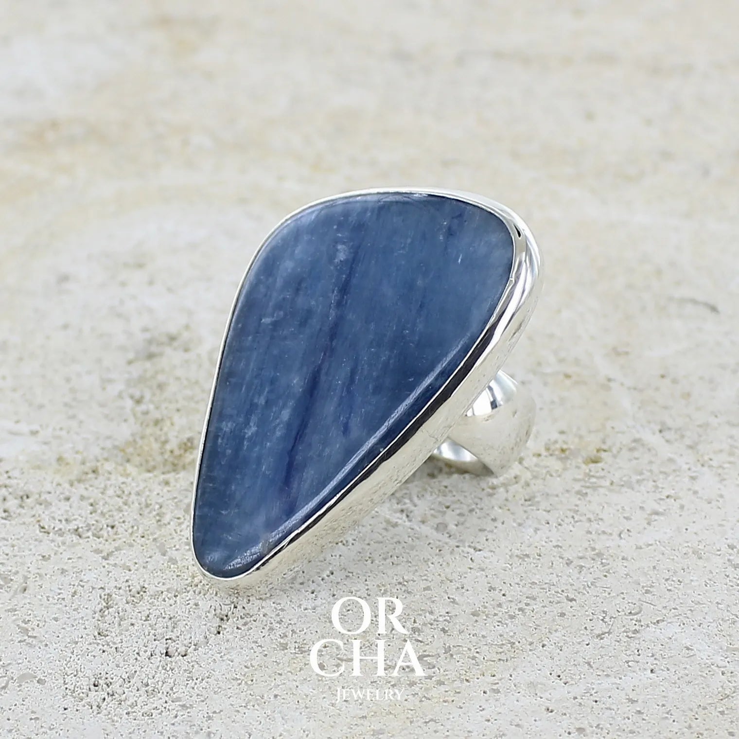 profil gauche d'une Bague longue et imposante pour femme en argent massif, sertie d'un cabochon de cyanite de couleur bleu jean nacré. Pierre taillée en forme de triangle de qualité translucide. Bijou unique réalisée en taille 58 par Orchajewelry
