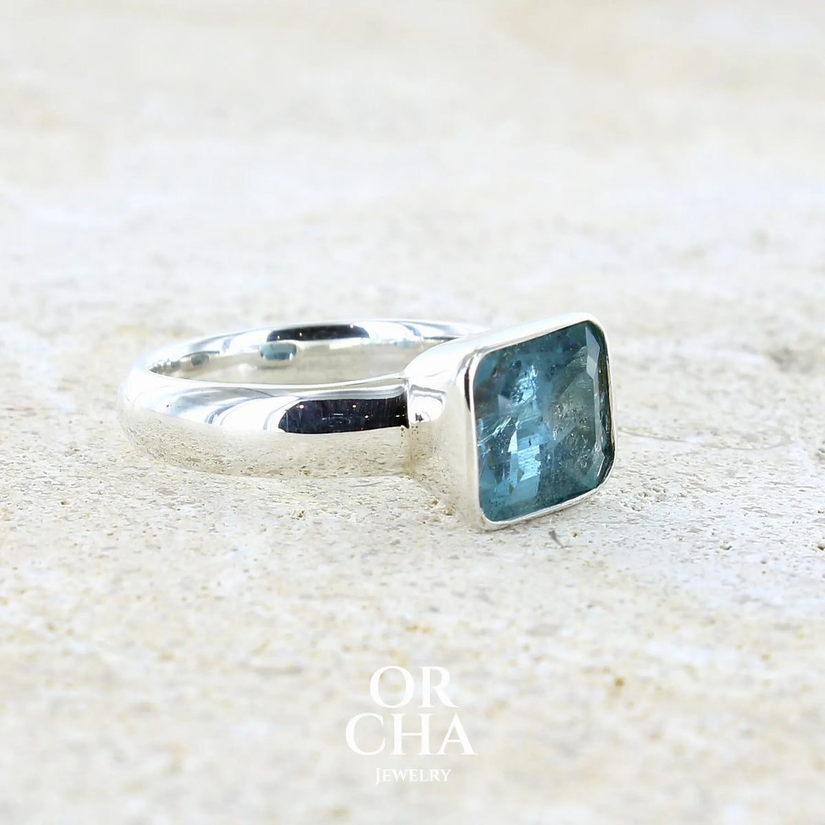 Profil d'une bague pour femme en argent massif sertie d'une aigue marine taillée de 4 carats de couleur bleue foncé profonde  intense et lumineuse, pierre transparente avec inclusions. Pierre naturelle facettée de forme rectangulaire. Bijoux unique réalisée en taille 56 par Orchajewelry 