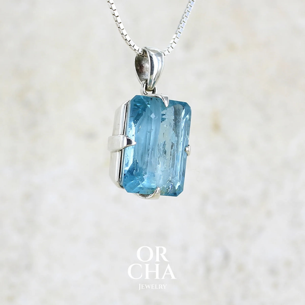 Profil droit d'un pendentif unisexe en argent massif sertie d'une aigue marine taillée de 17 carats de couleur bleu foncé profond et intense, pierre transparente avec de grosses inclusions. Pierre naturelle facettée de forme rectangulaire. Bijoux unique réalisée par Orchajewelry