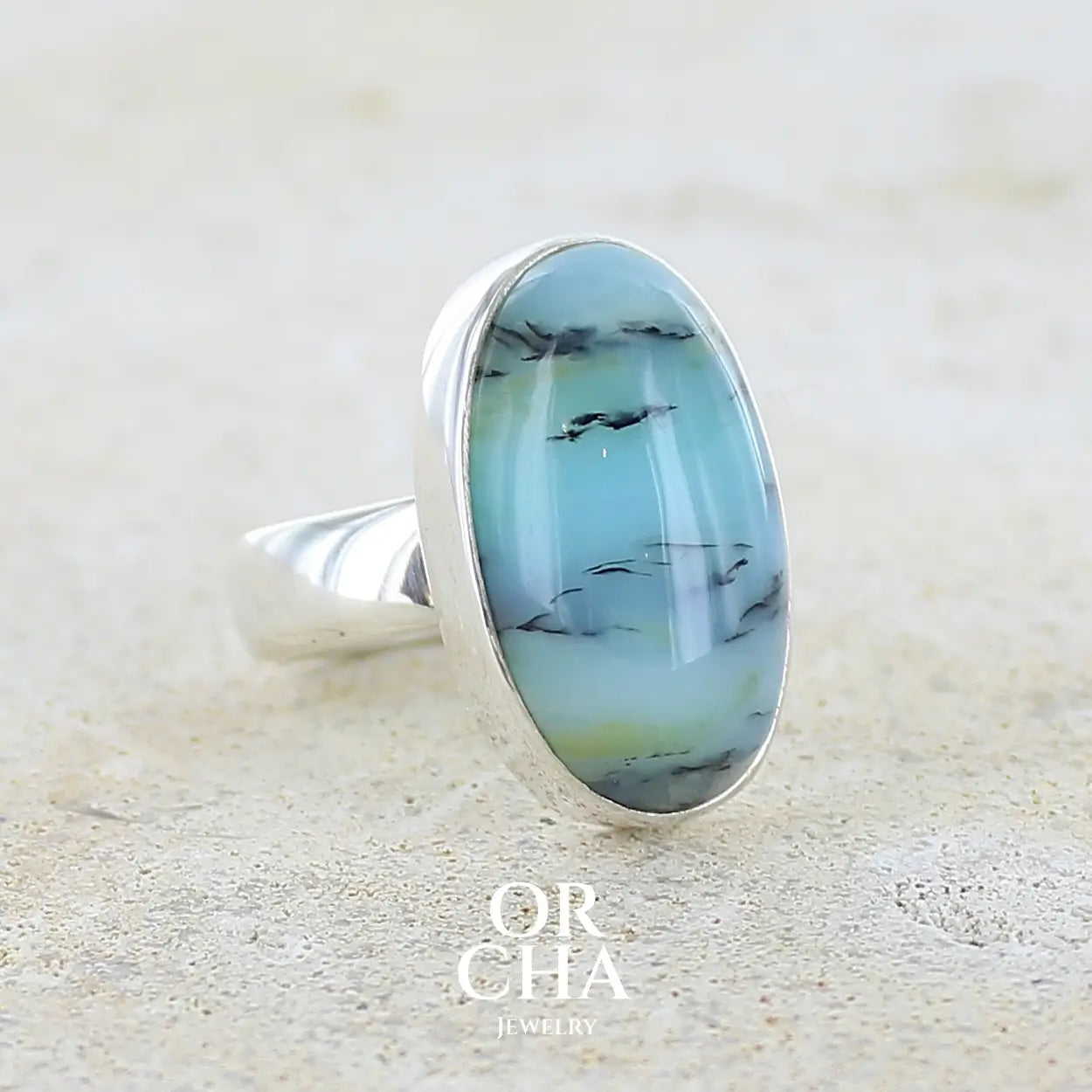 Profil droit d'une bague pour femme en argent massif, sertie d'un cabochon ovale d'opale bleue du Pérou de couleur bleu laiteux à inclusions de dendrites noires. Pierre naturelle de qualité opaque et translucide. Bijoux unique réalisé en taille 54,5 - OrchaJewelry