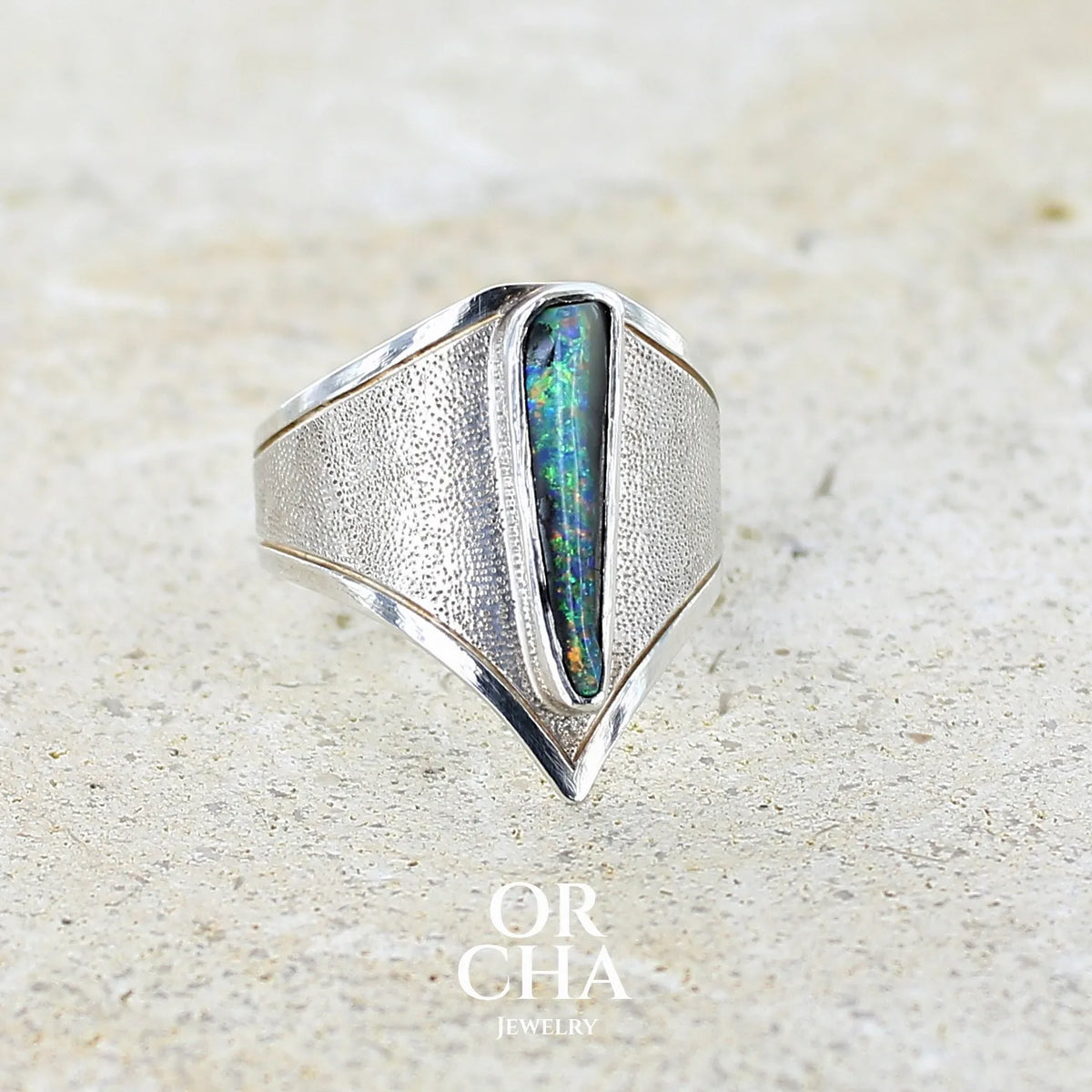 Profil droit d'une bague pour femme en argent massif 925 sertie d'une opale boulder aux feux multicolores bleus violet et verts. Cabochon d'opale massive naturelle taillée en forme d'aile. Pierre de qualité opaque. Bijoux unique réalisé en taille 57 par Orcha Jewelry.