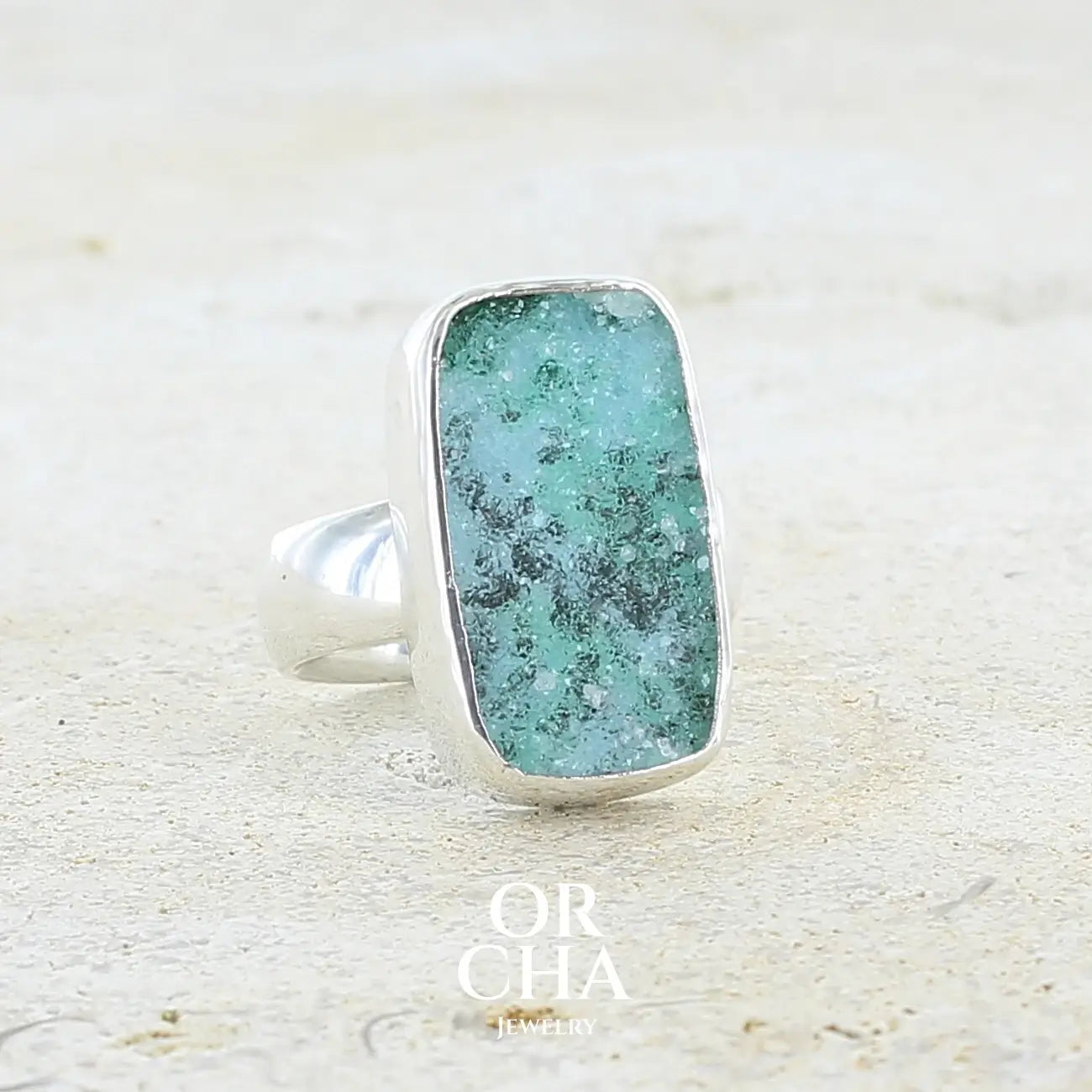 Profil droit d'une bague pour femme en argent massif sertie d'un magnifique gemsilica druzy: chrysocale solidifiée recouverte de fins cristaux de quartz scintillant. Pierre de qualité opaque taillée en tranche de forme rectangulaire. Pierre naturelle originaire de République dominicaine du Congo de couleur turquoise, verte et noire. Taille 56. Bijoux unique, éthique et durable présenté dans un coffret de notre marque, prêt à offrir. Livraison offerte, certificat d'authenticité, service client.