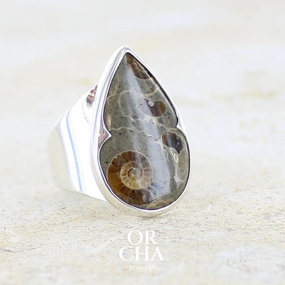 Profil droit d'une bague en argent massif 925 sertie d'un marbre de Marston poire aux ammonites fossiles brun caramel sur fond gris taupe. Pierre fossile ornementale naturelle originaire Marston Magna, dans le Somerset en Angleterre. Bijoux uniques réalisé en taille 55 - Orcha jewelry