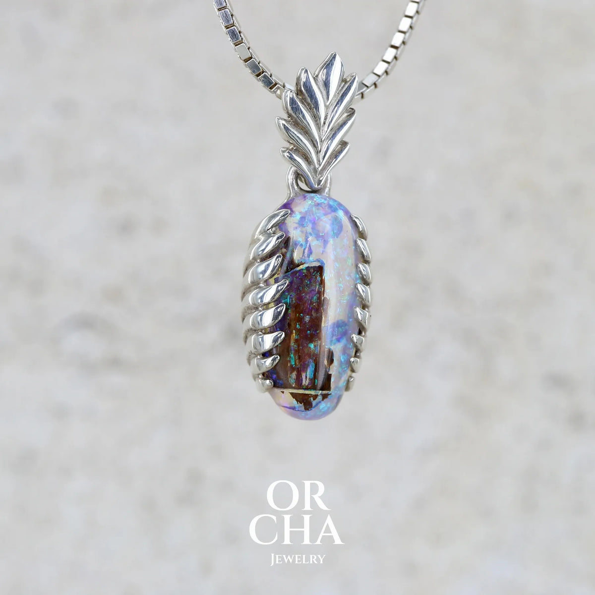 Profil droit d'un pendentif pour femme en argent massif 925 serti d'une opale cristal aux feux étoilés multicolores à dominante bleu violet et vert. Cabochon de 3,2 carats taillé de forme oval de qualité transparente. Bijou unique réalisé par Orchajewelry
