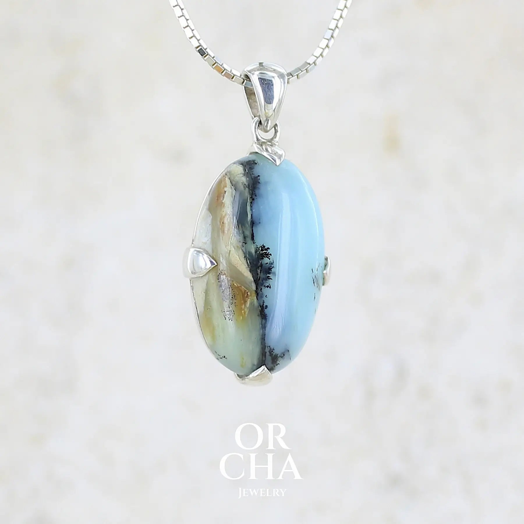 profil droit d'un pendentif pour femme et homme en argent massif, sertie d'un cabochon ovale d'opale bleue du Pérou de couleur bleu laiteux à inclusions de dendrites paysages noires et de roche mère marron. Pierre opaque et translucide. Bijoux unique, éthique et durable présenté dans un coffret de notre marque, prêt à offrir. Livraison offerte, certificat d'authenticité, service client.