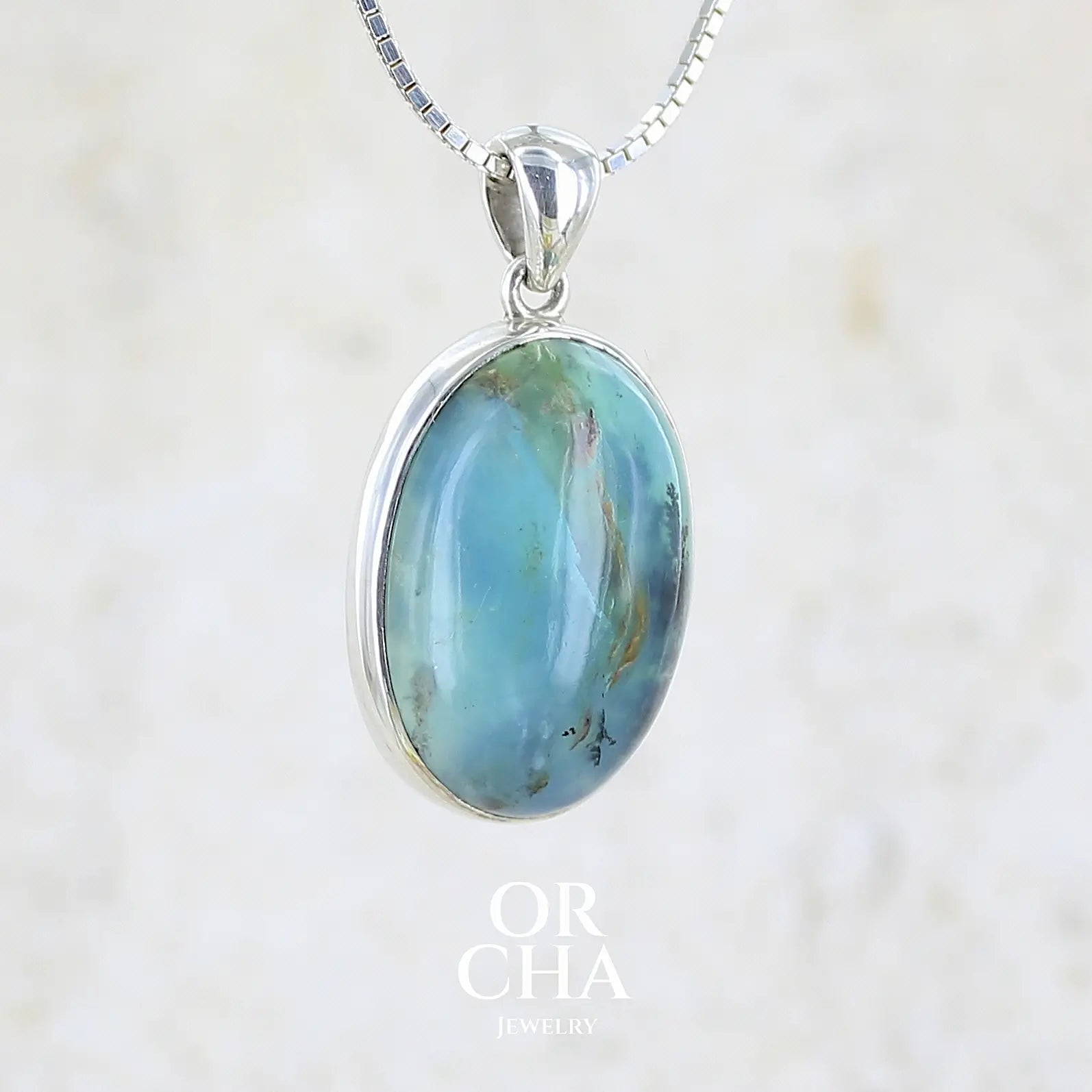 profil droit d'un pendentif en argent massif, sertie d'un cabochon ovale d'opale bleue du Pérou de couleur bleu laiteux foncé à inclusions de dendrites paysages noires et de roche mère marron. Pierre opaque et translucide. Bijoux unique, éthique et durable présenté dans un coffret de notre marque, prêt à offrir. Livraison offerte, certificat d'authenticité, service client.