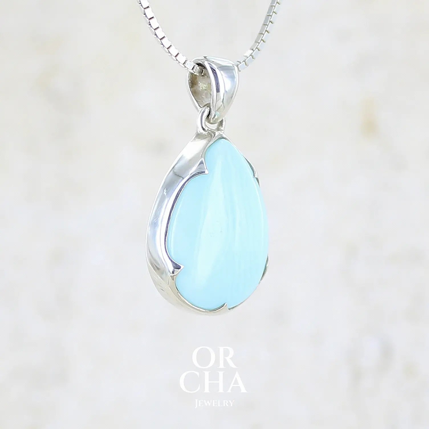 profil droit d'un pendentif pour femme en argent massif, sertie d'un cabochon d'opale bleue du Pérou de couleur bleu ciel clair. Pierre en forme de goutte. Pierre opaque. Bijoux unique, éthique et durable présenté dans un coffret de notre marque, prêt à offrir. Livraison offerte, certificat d'authenticité, service client.