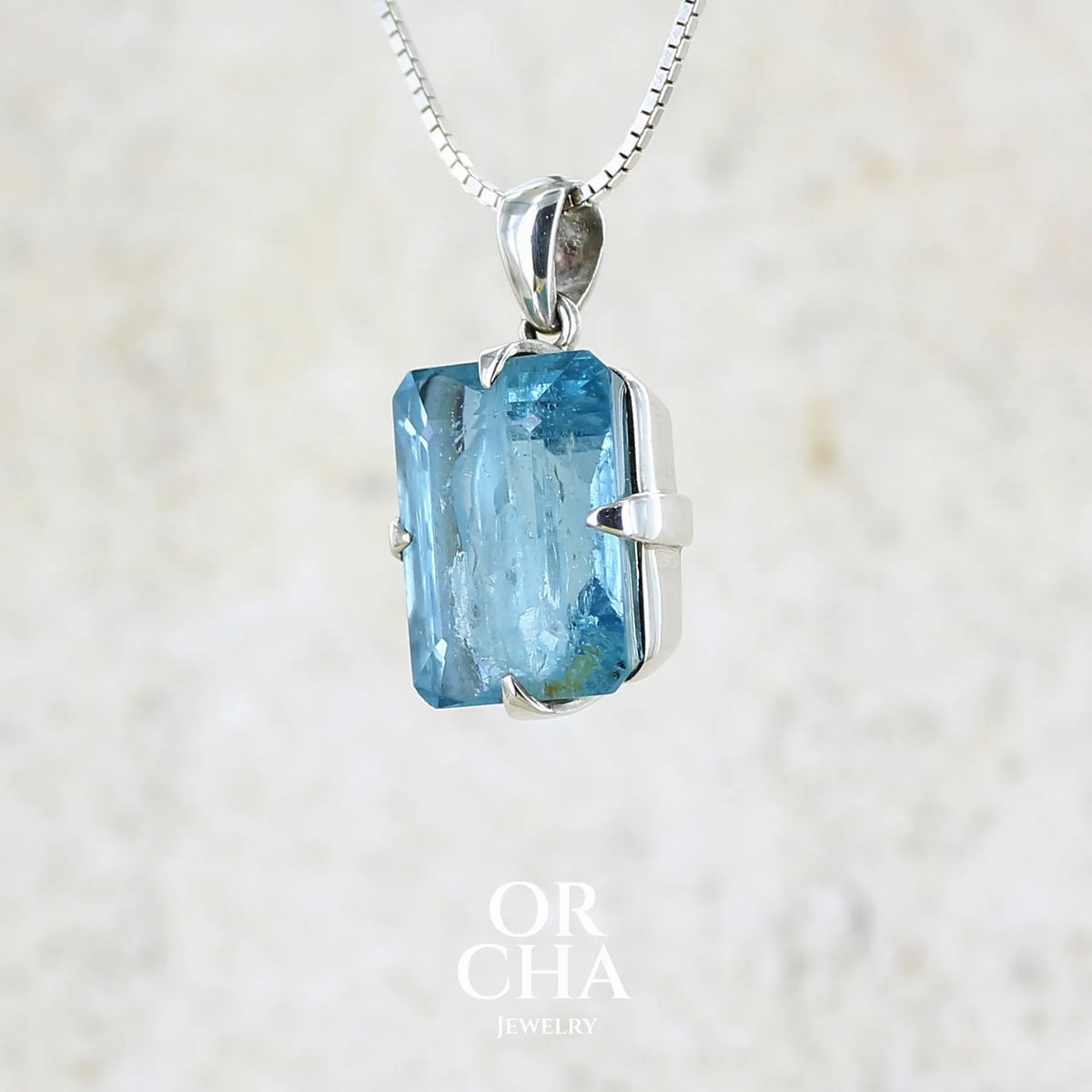 Profil gauche d'un pendentif unisexe en argent massif sertie d'une aigue marine taillée de 17 carats de couleur bleu foncé profond et intense, pierre transparente avec de grosses inclusions. Pierre naturelle facettée de forme rectangulaire. Bijoux unique réalisée par Orchajewelry