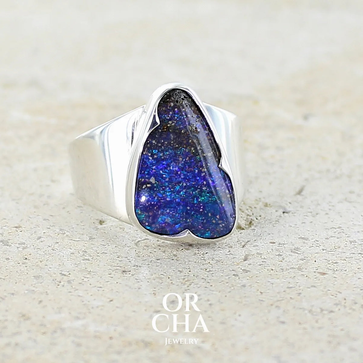 Profil gauche d'une bague pour femme en argent massif 925 sertie d'une opale boulder aux feux multicolores bleus violet et verts. Cabochon d'opale massive naturelle taillée en forme d'aile. Pierre de qualité opaque. Bijoux unique réalisé en taille 58 par Orcha Jewelry.