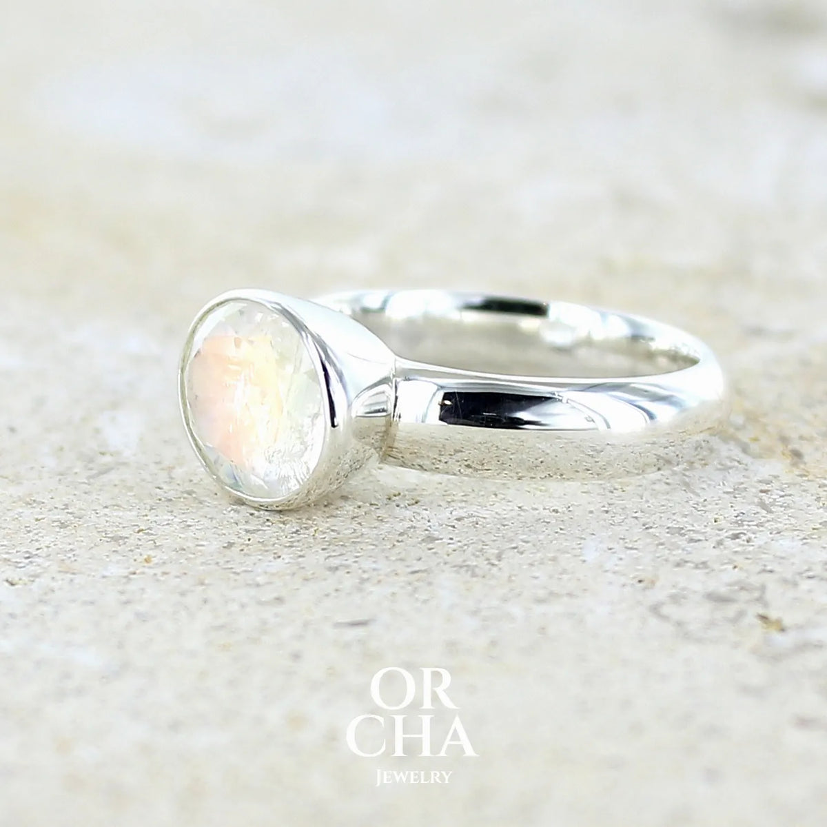 Profil gauche d'une Bague cocktail pour femme en argent massif 925 sertie d'une pierre de lune arc en ciel de Madagascar taillée de 2,5 carats incolore aux reflets bleutés et arc en ciel. Pierre transparente avec inclusions. Bijoux unique réalisée en taille 56 par Orchajewelry