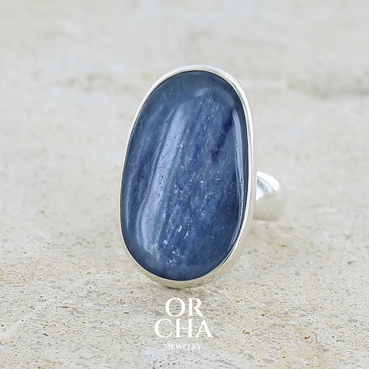 Profil gauche d'une bague pour femme en argent massif sertie d'un cabochon de cyanite de couleur bleu jean nacré. Pierre translucide à inclusions de forme ovale arrondie. Bijou unique réalisée en taille 58,5 par Orchajewelry