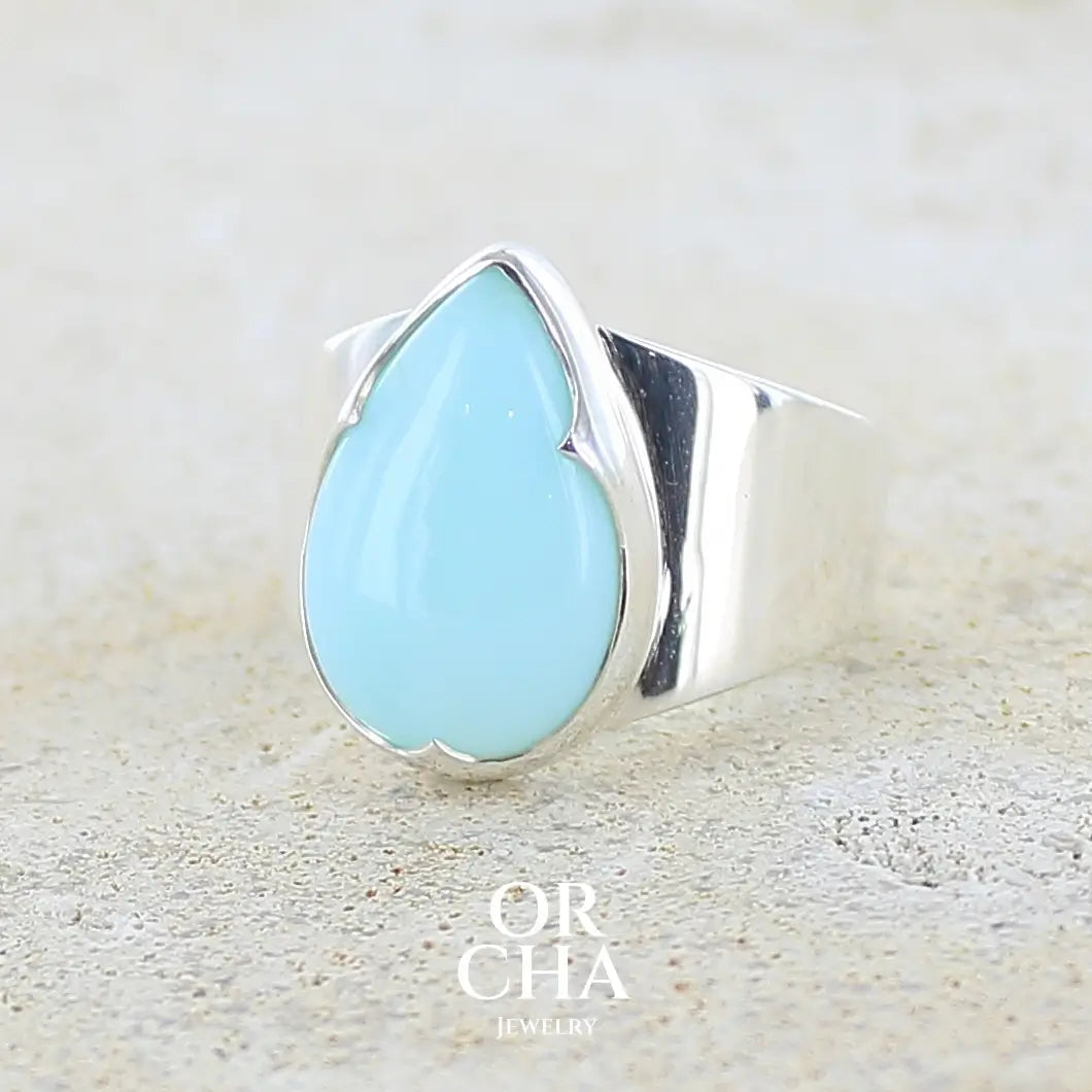 Profil gauche d'une bague pour femme en argent massif, sertie d'un cabochon d'opale bleue du Pérou de couleur bleu ciel. Pierre taillée en forme de goutte de qualité opaque. Bijou unique de taille 56