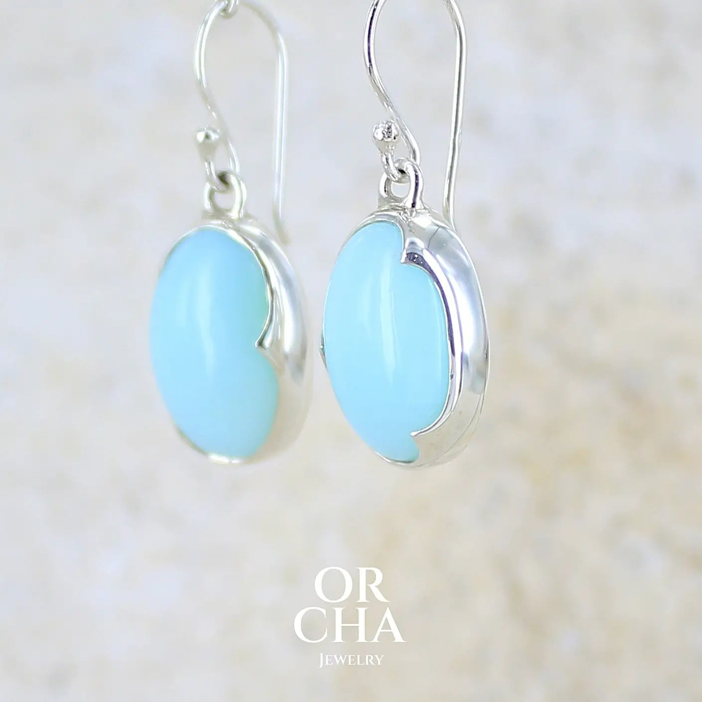 profil gauche boucles d'oreilles pendantes en argent massif serties d'opale bleue du Pérou. Pierres cabochon taillée en ovale de qualité opaque. Pierre naturelle de couleur bleu ciel. Bijoux unique, éthique et durable présenté dans un coffret de notre marque, prêt à offrir. Livraison offerte, certificat d'authenticité, service client.