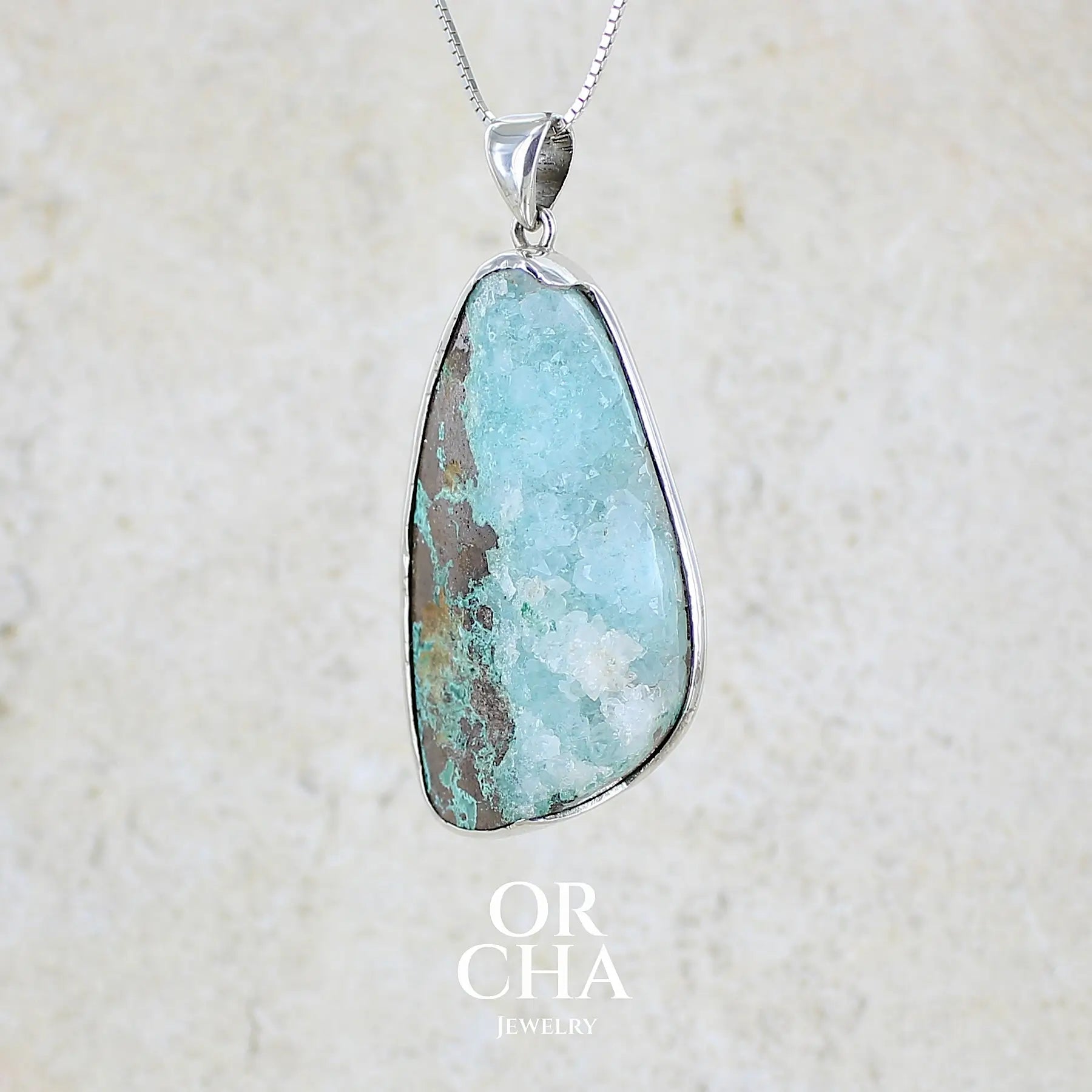 profil gauche d'un pendentif en argent massif serti d'un magnifique gemsilica druze: chrysocolle silicifiée recouverte de fins cristaux de quartz scintillant. Pierre de qualité opaque brute en forme de goutte. Pierre naturelle originaire du Mexique de couleur bleue ciel turquoise claire.
