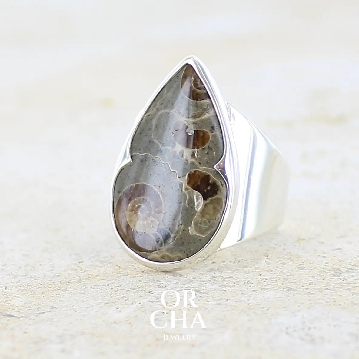 Profil gauche d'une bague en argent massif 925 sertie d'un marbre de Marston poire aux ammonites fossiles brun caramel sur fond gris taupe. Pierre fossile ornementale naturelle originaire Marston Magna, dans le Somerset en Angleterre. Bijoux uniques réalisé en taille 55 - Orcha jewelry