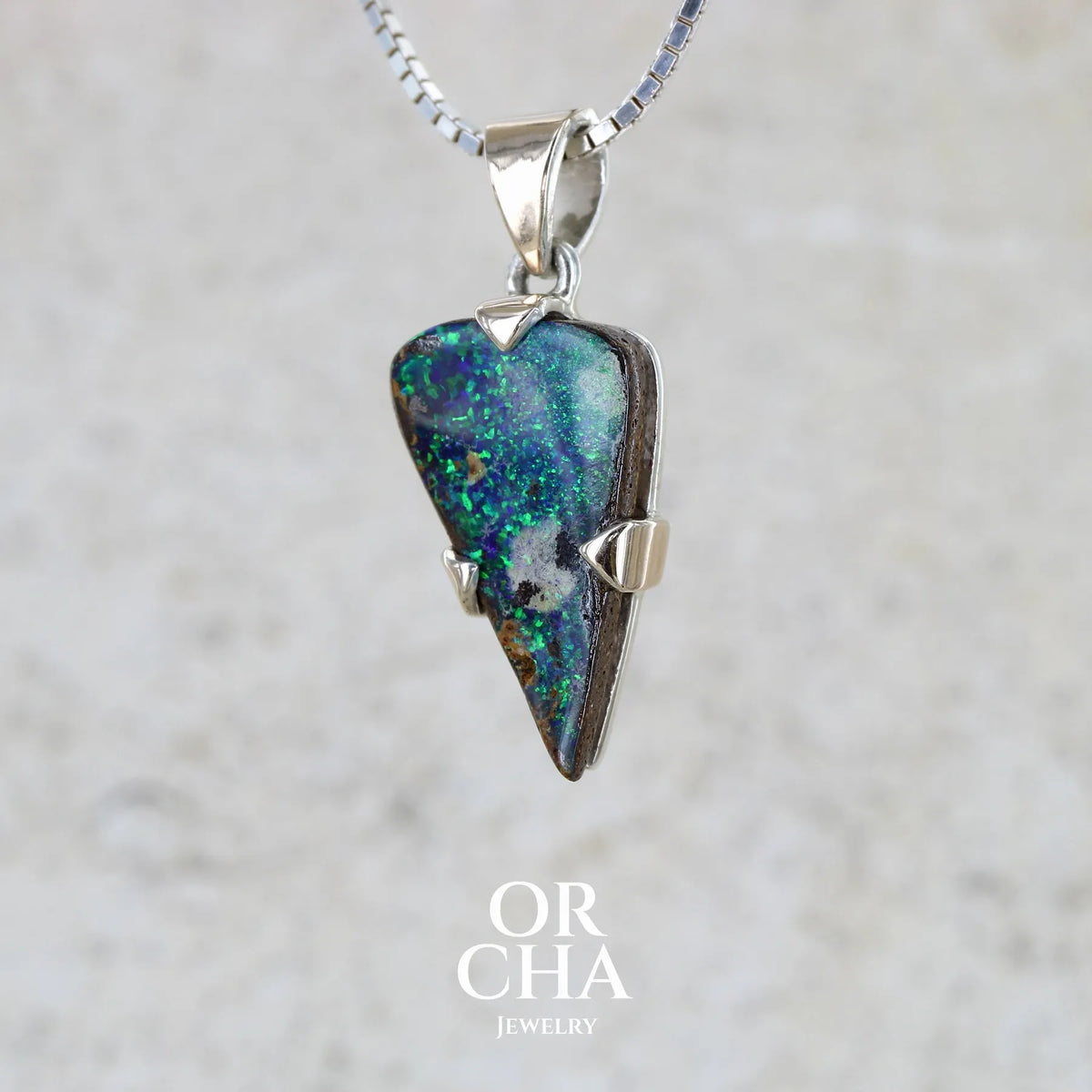 profil gauche d'un pendentif pour homme en or 9k et argent massif 925 serti d'une opale boulder aux feux multicolores bleus et verts. Tranche d'opale massive naturelle taillée en forme d'aile. Pierre de qualité opaque originaire d'Australie. Bijoux unique par Orcha Jewelry.