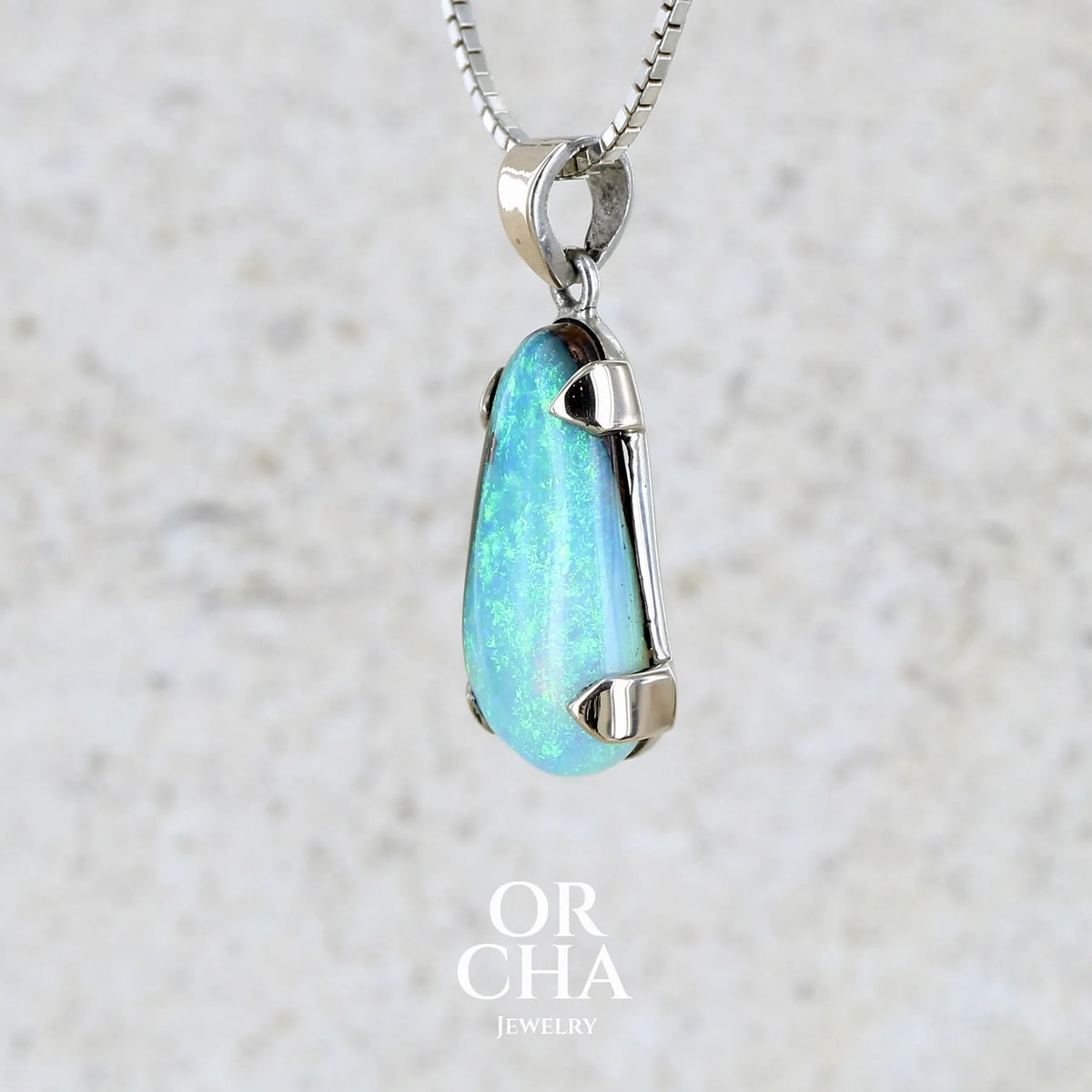 profil gauche d'un pendentif pour femme en or 9k et argent massif serti d'une opale boulder cristal aux feux étoilés multicolores à dominantes bleu turquoise. Cabochon de 7 carat taillé en forme de goutte de qualité translucide. Opale massive australienne. Bijou unique réalisé par Orchajewelry