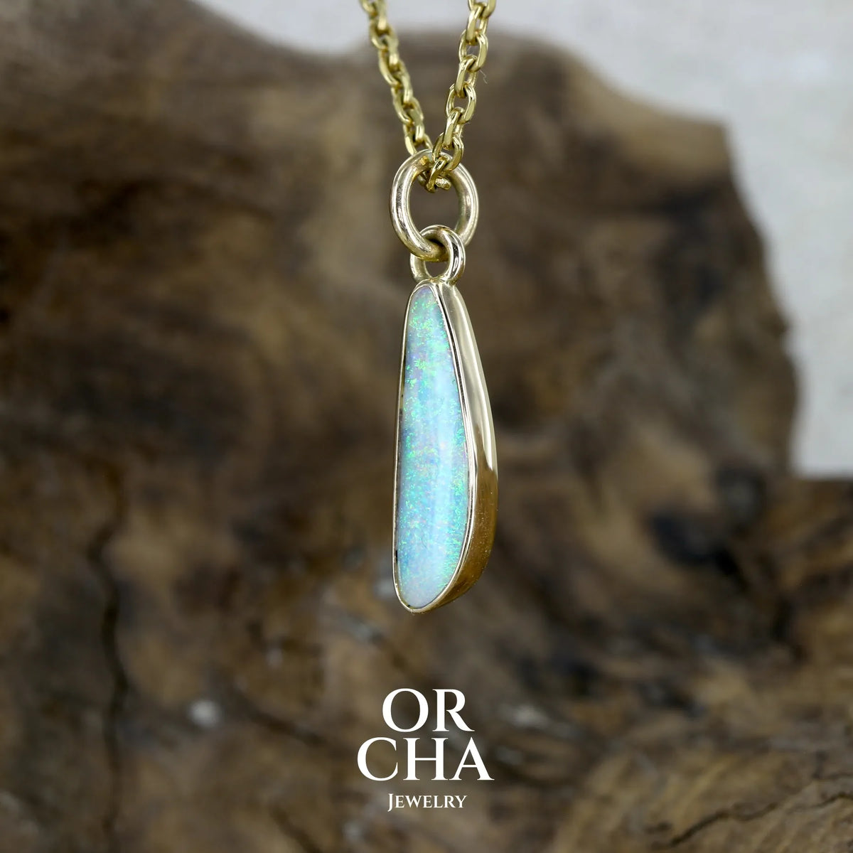 profil gauche serti d'un pendentif pour femme en or jaune massif 18k serti d'une opale cristal aux feux étoilés multicolores à dominantes vert turquoises. Cabochon de 1 carat taille en forme de goutte de qualité transparente. Bijou unique réalisé par Orchajewelry