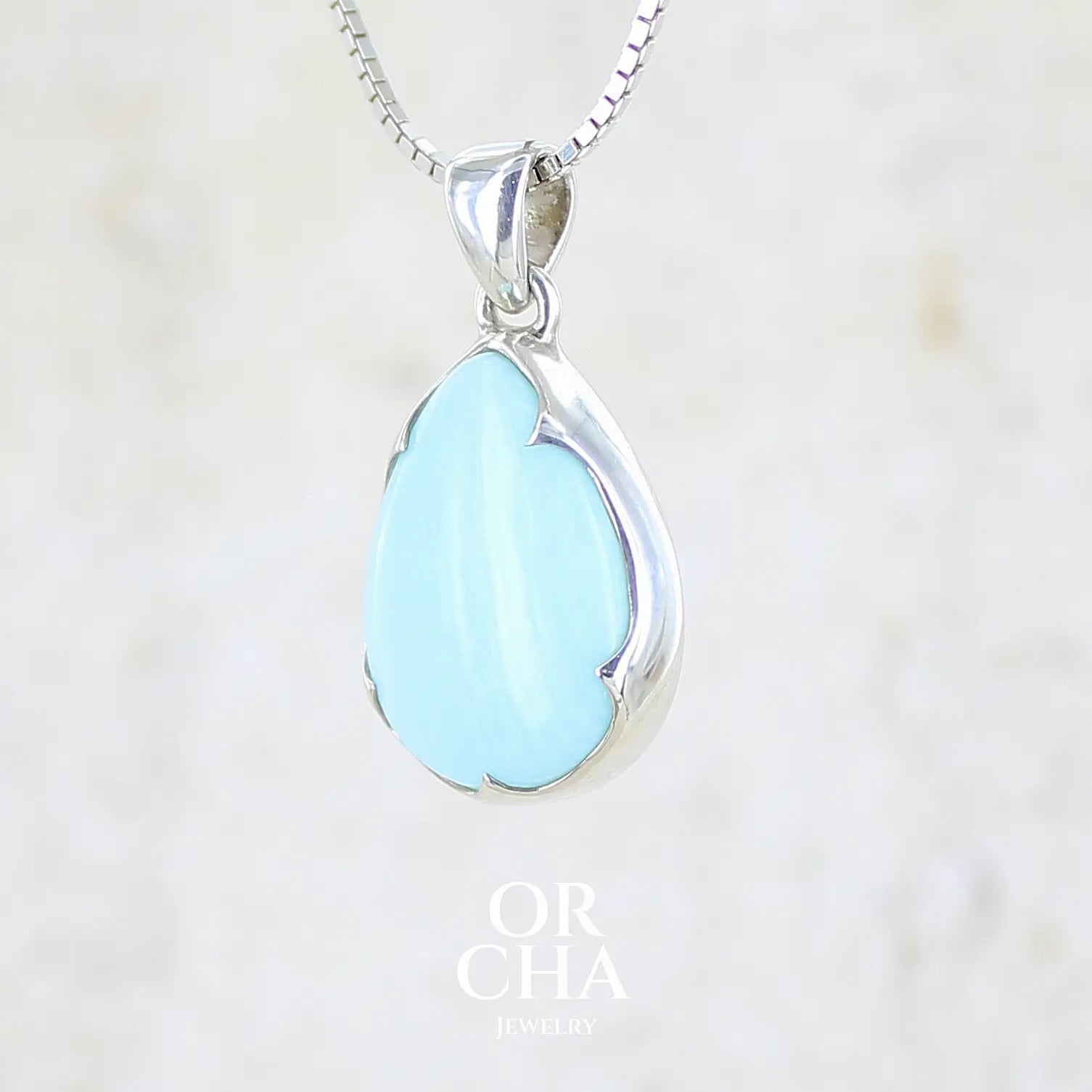 profil gauche d'un pendentif pour femme en argent massif, sertie d'un cabochon d'opale bleue du Pérou de couleur bleu ciel clair. Pierre en forme de goutte. Pierre opaque. Bijoux unique, éthique et durable présenté dans un coffret de notre marque, prêt à offrir. Livraison offerte, certificat d'authenticité, service client.
