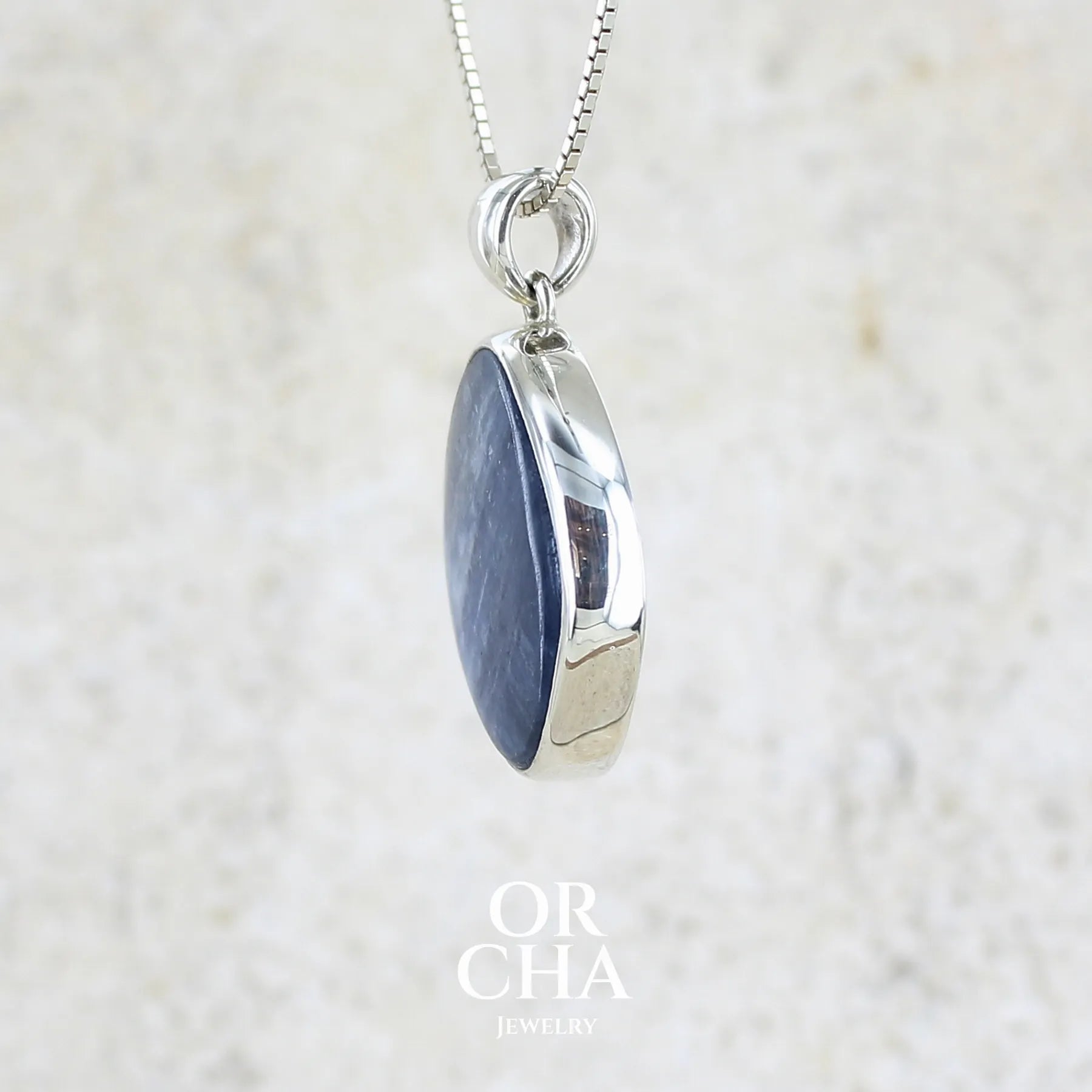 Profil d'un pendentif en argent massif serti d'un cabochon de cyanite de couleur bleue jeans nacré. Pierre de qualité opaque comportant des inclusions. Bijoux unique par Orcha Jewelry