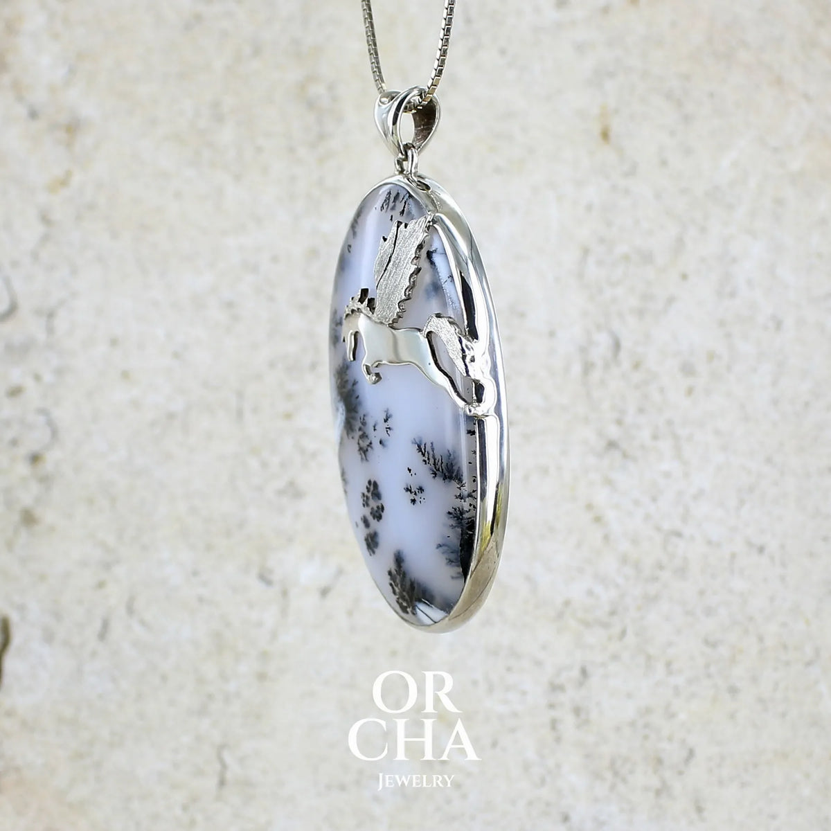 profil d'un pendentif en argent massif sertie d'un grand cabochon de forme ovale d'agate dendritique de couleur blanc pur et noir. Pierre opaque à translucide à inclusions paysages de dendrites de manganèse noires contrastées. Bijou unique illustré d'un cheval ailé réalisé par Orchajewelry