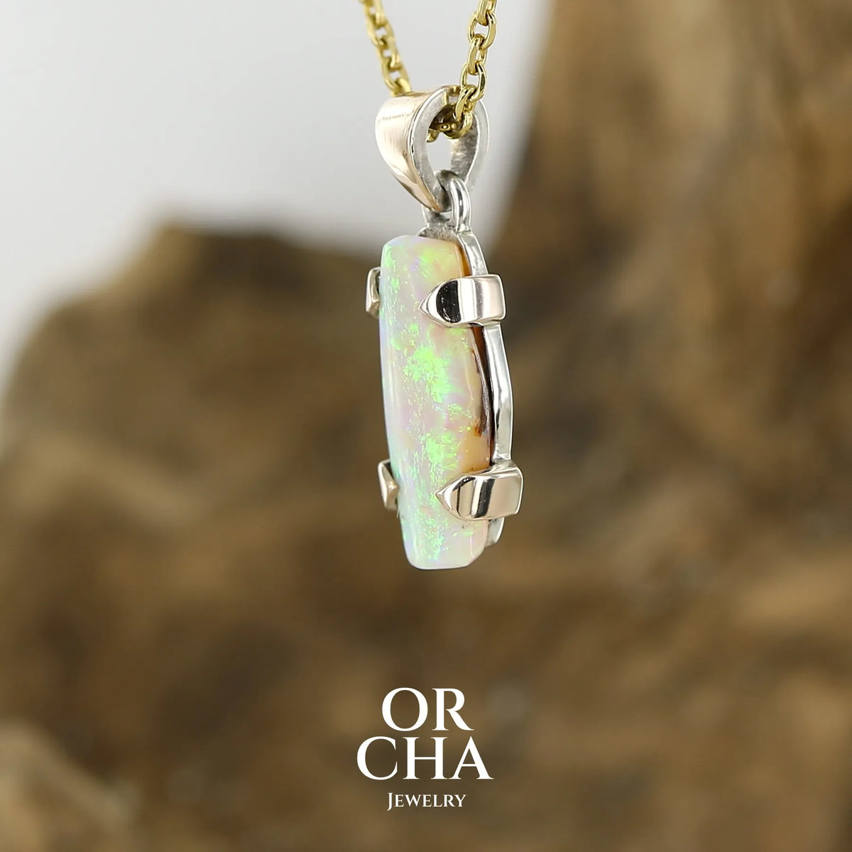Profil d'un pendentif pour femme en or 9k et argent massif serti d'une opale cristal aux feux étoilés multicolores à dominantes vert et jaune. Cabochon de 3 carat de forme libre de qualité translucide. Opale australienne. Bijou unique réalisé par Orchajewelry