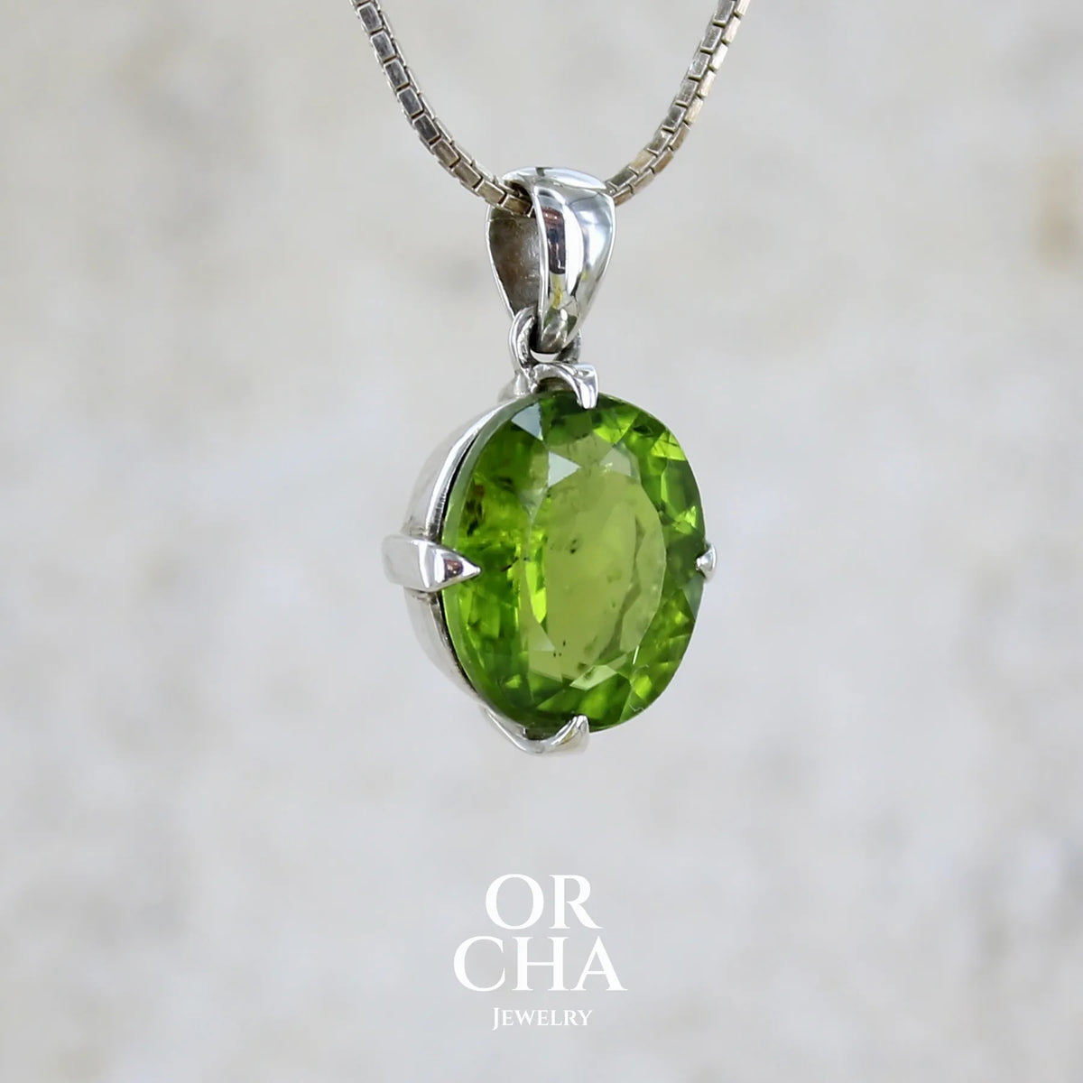 Profil d'un pendentif pour femme en argent massif serti d'un péridot de couleur vert olive doré intense. Pierre taillée, de forme ovale, transparente présentant de nombreuse inclusions. Bijou unique réalisé par Orchajewelry