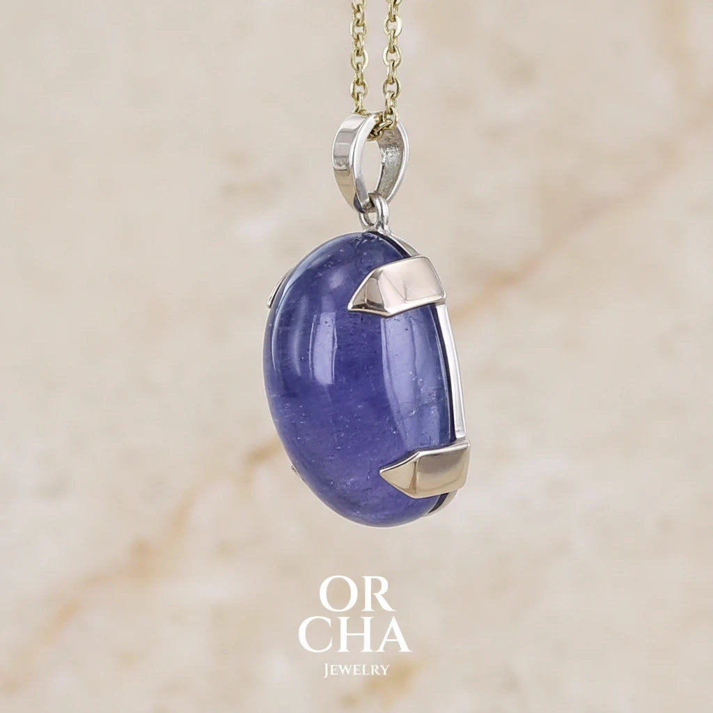 détail de sertissure d'un pendentif en or 9k et argent massif serti d'un cabochon de Tanzanite de 46,3 carats, de couleur bleu lavande foncé profond et intense. Pierre transparente présentant des inclusions. Pierre ayant subit un traitement de chauffe, traitement admis et fréquent en gemmologie pour ce type de pierre . Bijoux unique, éthique et durable présenté dans un coffret de notre marque, prêt à offrir. Livraison offerte, certificat d'authenticité, service client.
