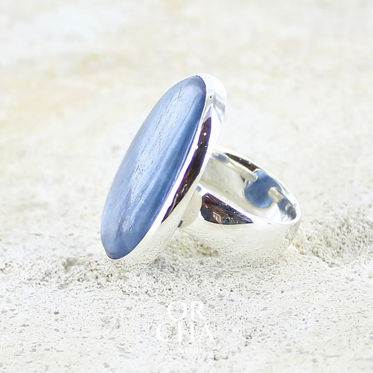 Détail du sertissage d'une bague pour femme en argent massif sertie d'un cabochon de cyanite de couleur bleu jean irisée. Pierre translucide à inclusions. Bijou unique réalisée en taille 56 par Orcha Jewelry