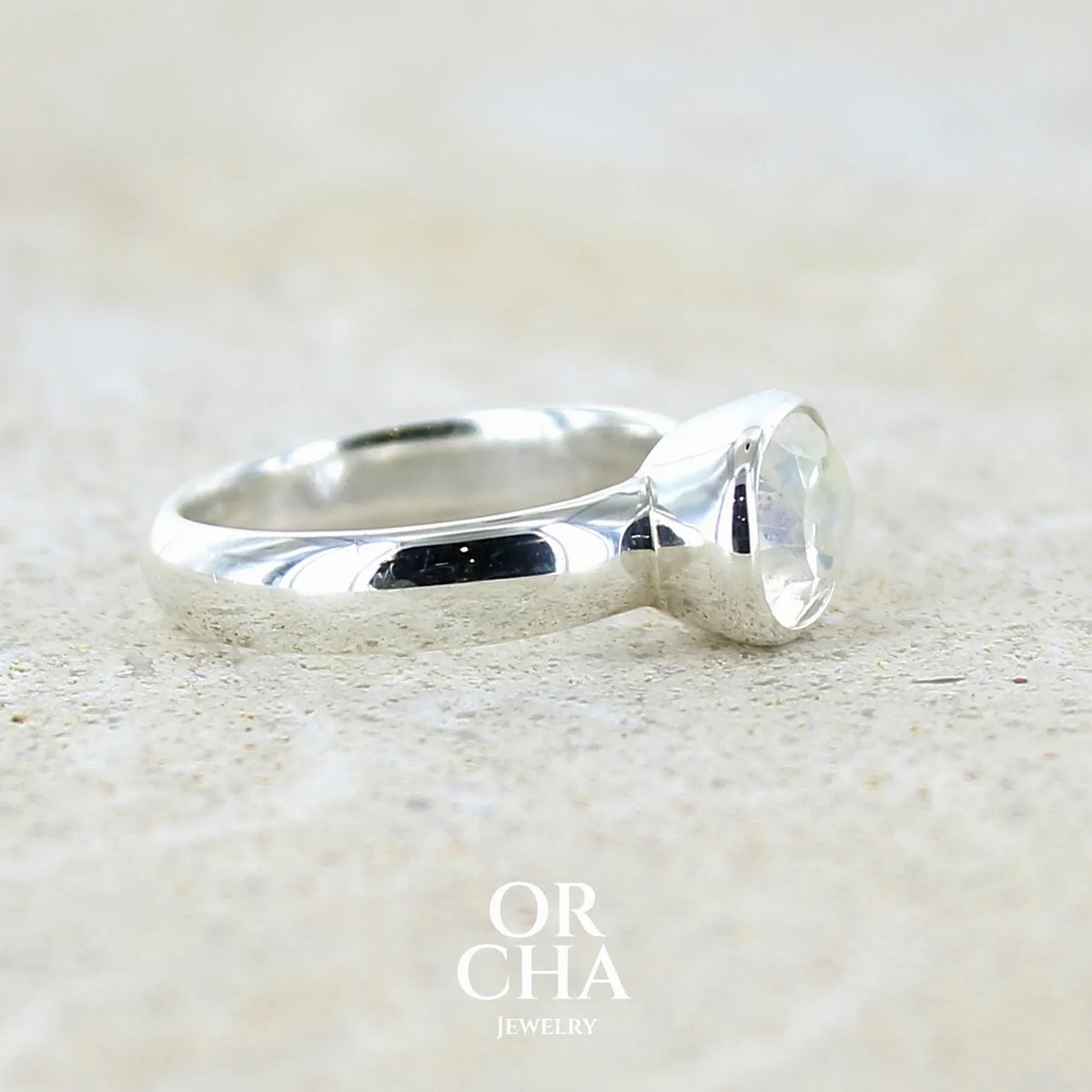 Détail du sertissage d'une bague cocktail pour femme en argent massif 925 sertie d'une pierre de lune de Madagascar taillée de 2,18 carats, pierre incolore aux reflets orangés et arc en ciel. Pierre transparente avec inclusions. Bijoux unique réalisé en taille 52 par Orcha Jewelry