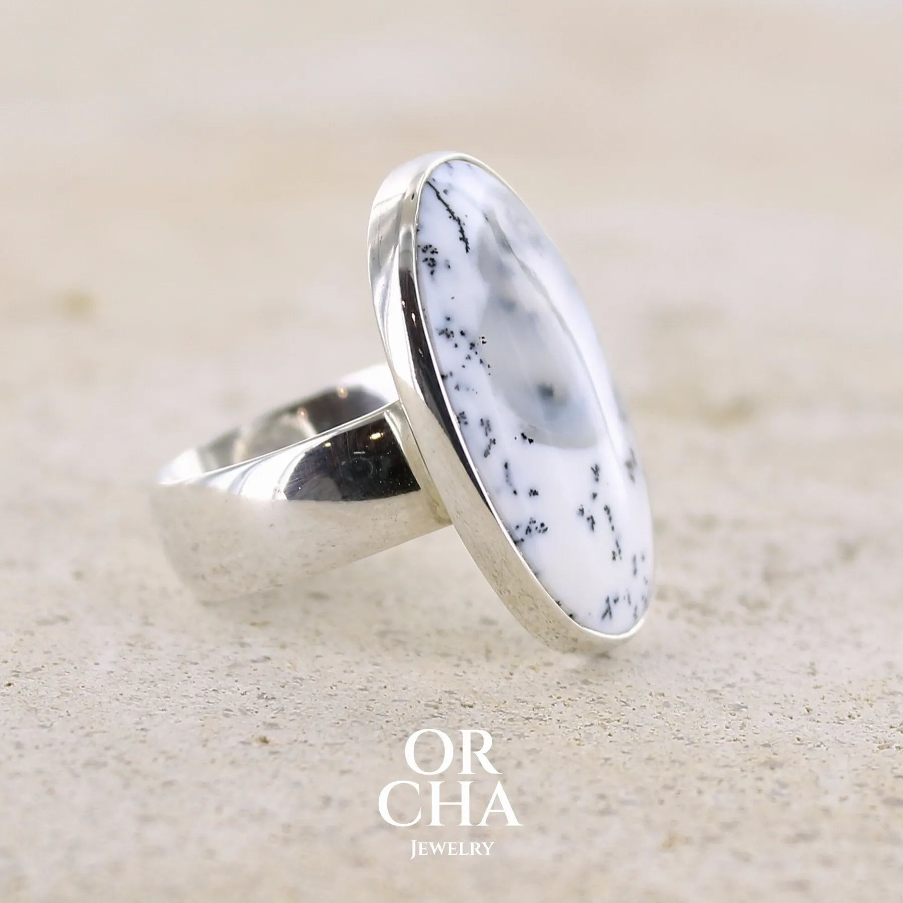 Détail du sertissage d'une bague pour femme en argent massif sertie d'un cabochon ovale d'agate dendritique de couleur blanc pur et noir. Pierre paysage opaque translucide à inclusions de dendrites de manganèse noires contrastées. Bijou unique réalisée en taille 52 par Orchajewelry