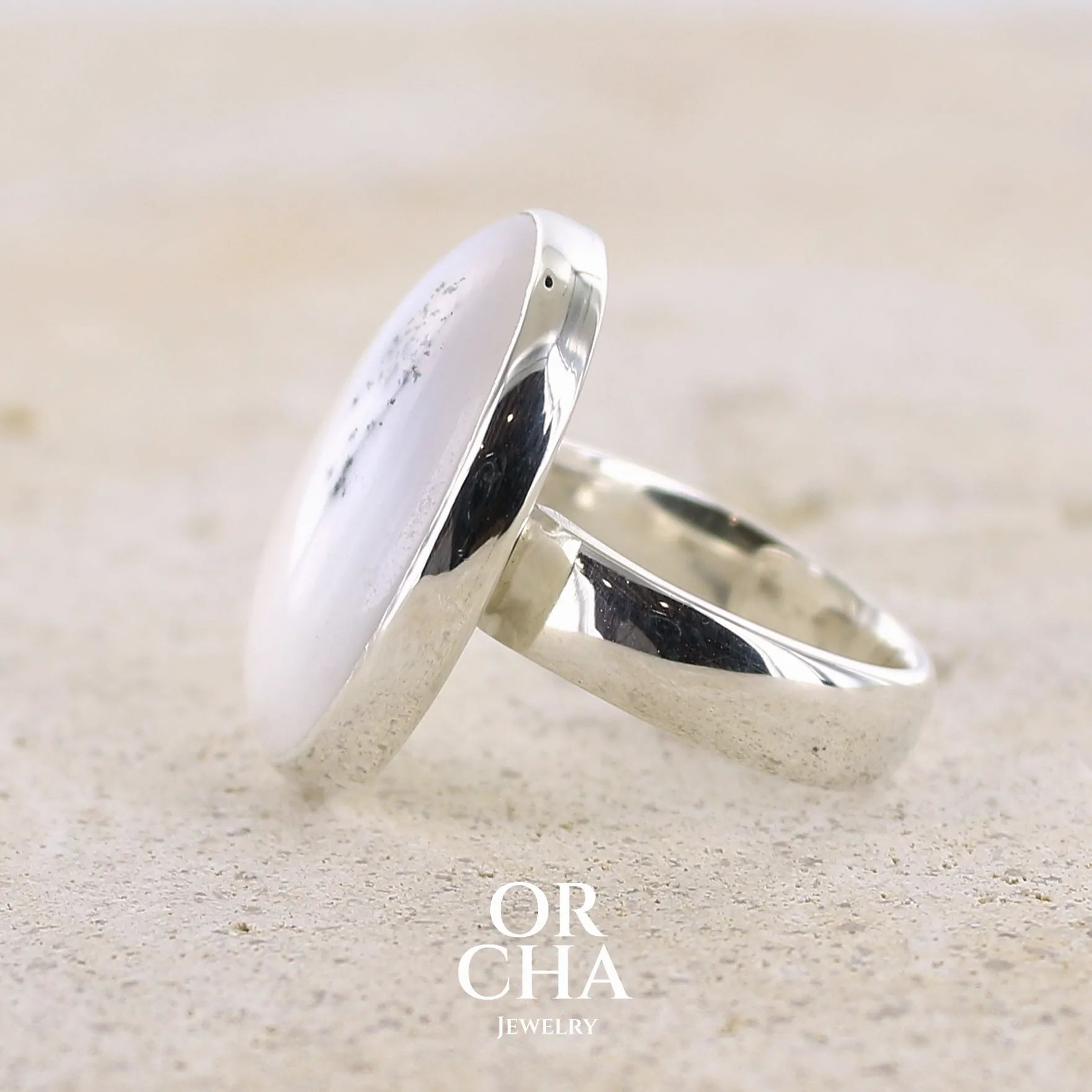 sertissage d'une bague pour femme en argent massif sertie d'un cabochon ovale d'agate dendritique de couleur blanc pur. Pierre opaque translucide à inclusions de dendrites de manganèse noires contrastées. Bijou unique réalisée en taille 56,5 par Orchajewelry